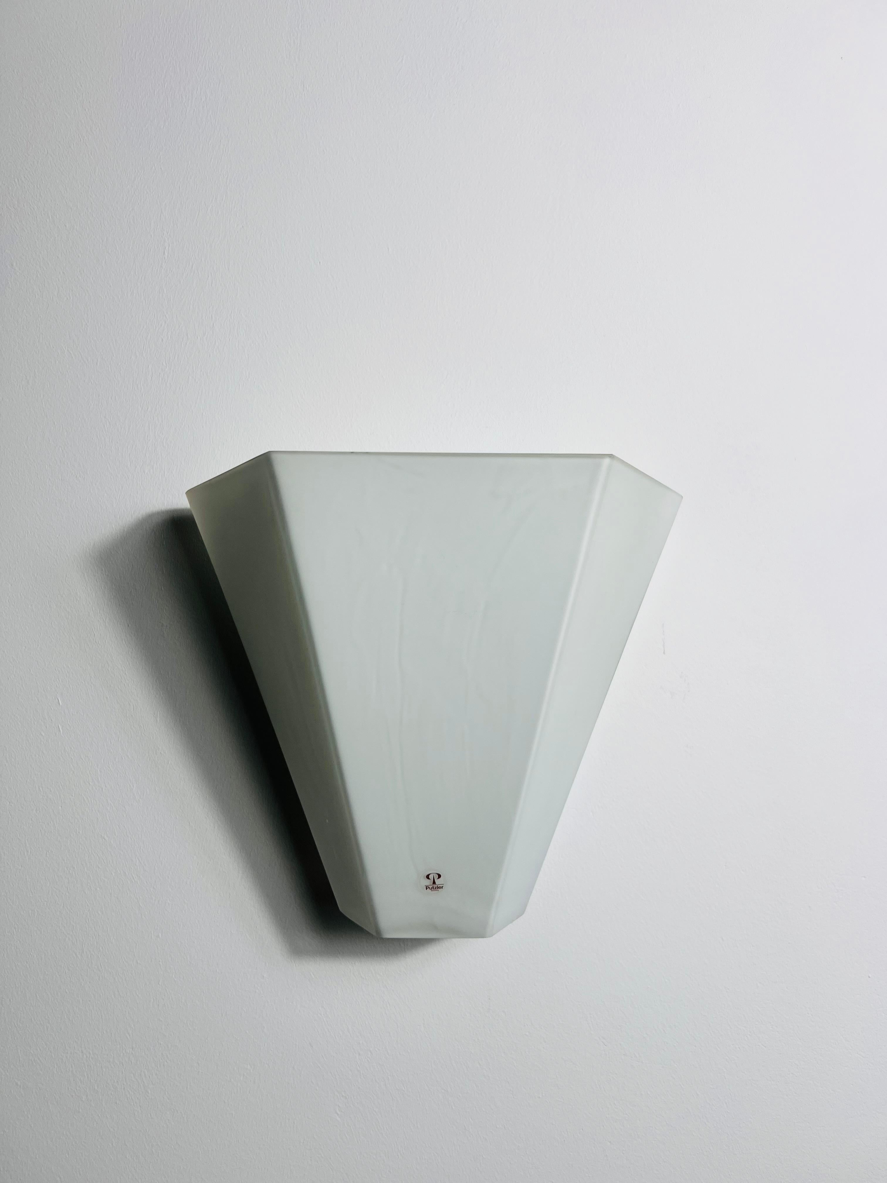 Diese elegante achteckige Wandleuchte wurde in den 1970er Jahren von Peill & Putzler entworfen und ist aus hochwertigem Opalglas gefertigt. Sein raffiniertes, luxuriöses Design wertet jeden Innenraum mühelos auf. Die Lampe strahlt ein weiches,