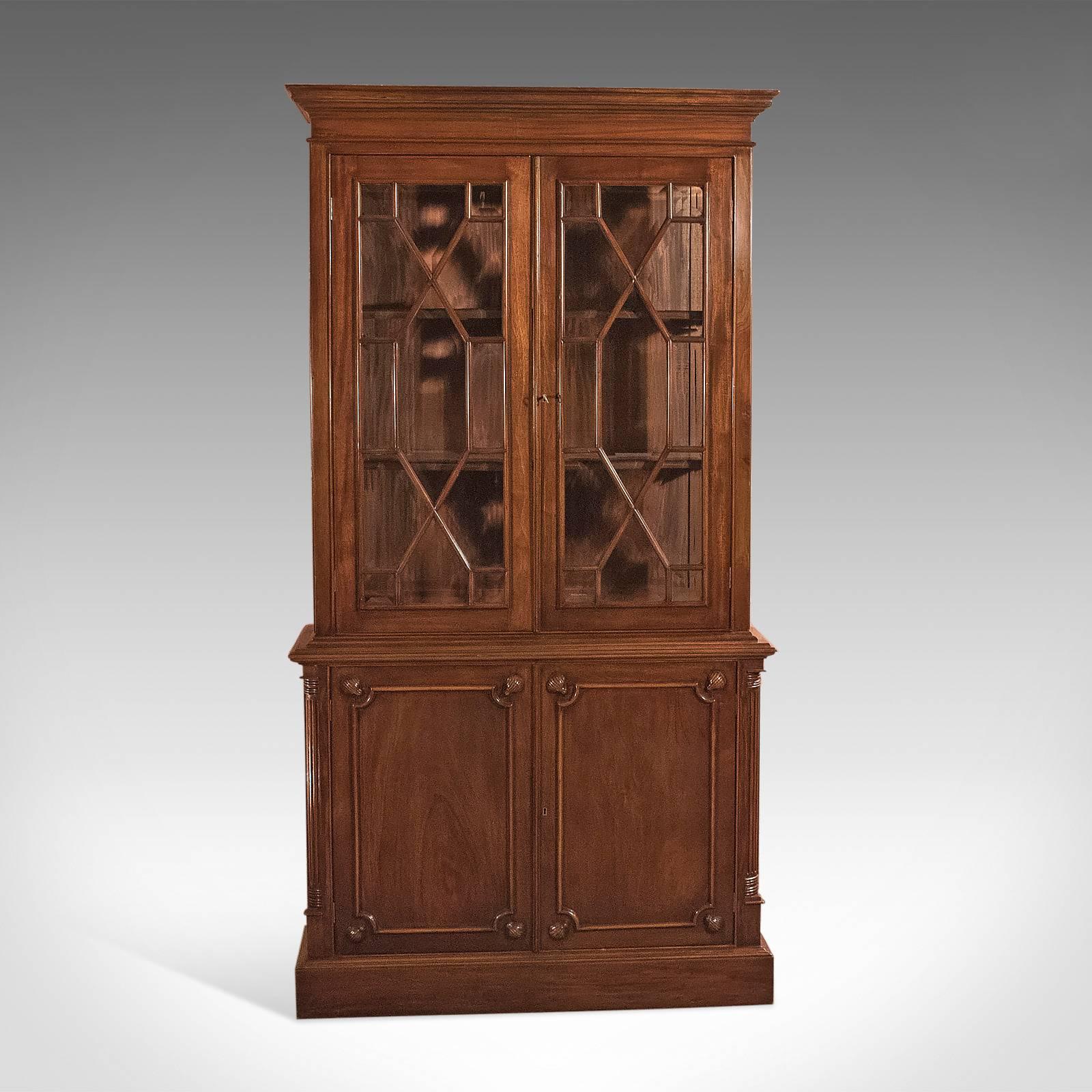 This is a bespoke mahogany bookcase cabinet in the Georgian taste.

Raised on a continues plinth with moulding finish
Two-door lower cabinet
Field panels with carved clam shell appliqué
Receded quarter column corner details
Single removable
