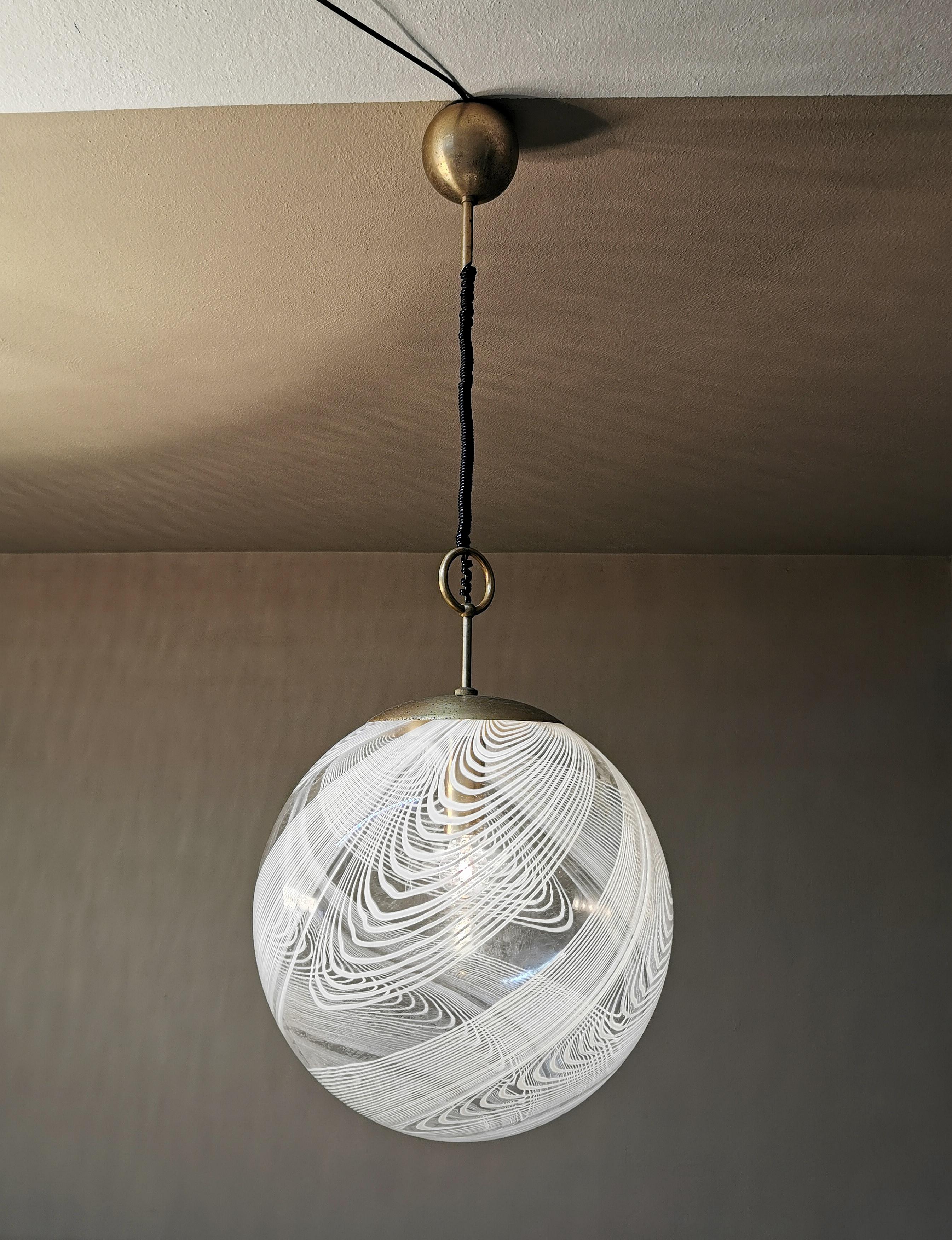 Pendant lamp with one light in white Murano glass by Venini with a spherical shape with particular processing of intertwining designs. Structure in golden metal. Italy, 1970.