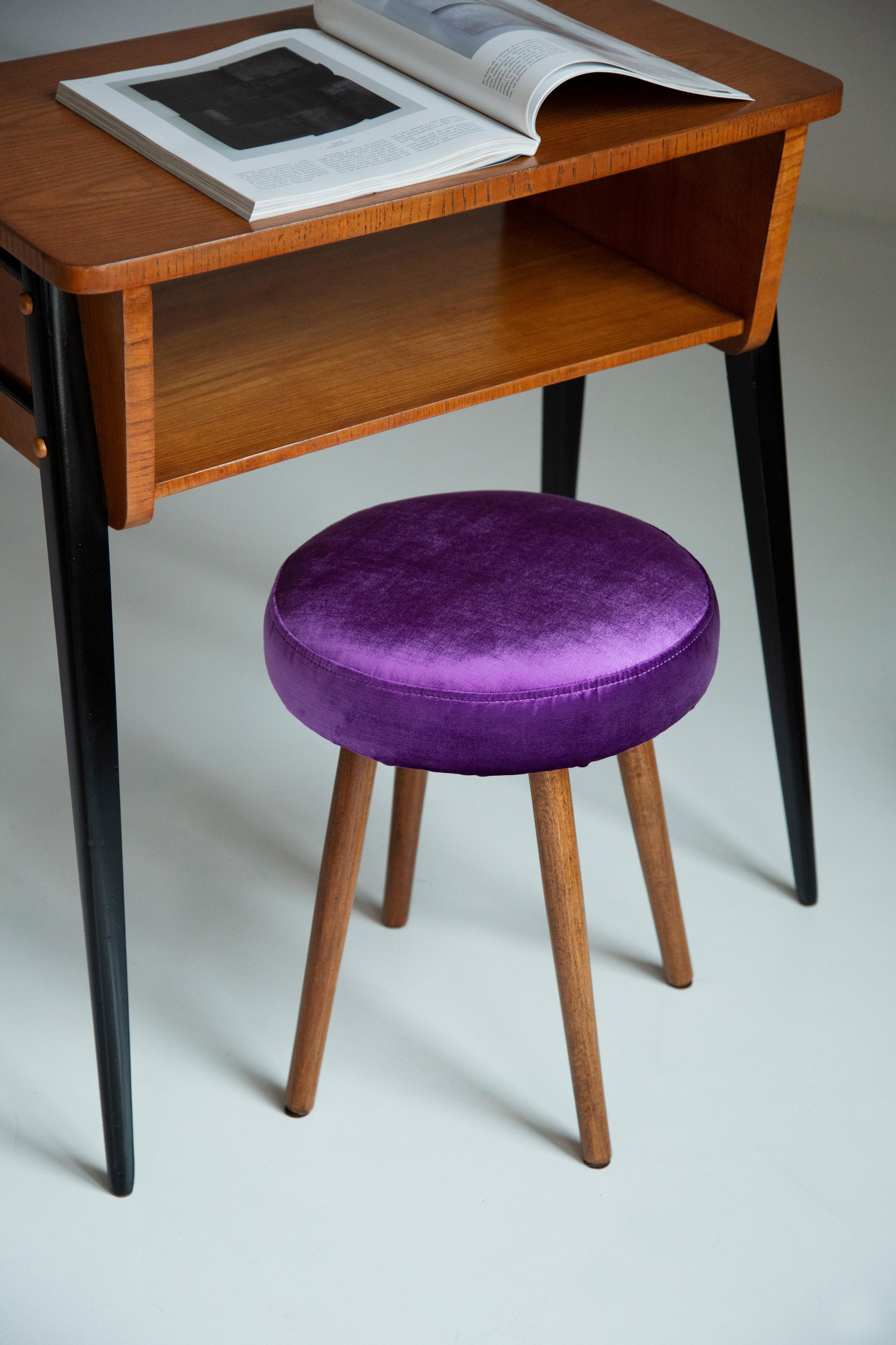 Tabouret du tournant des années 1960 et 1970. Magnifique tapisserie en velours de couleur violette brillante. Le tabouret est composé d'une partie rembourrée, d'un siège et de pieds en bois se rétrécissant vers le bas, caractéristiques du style des