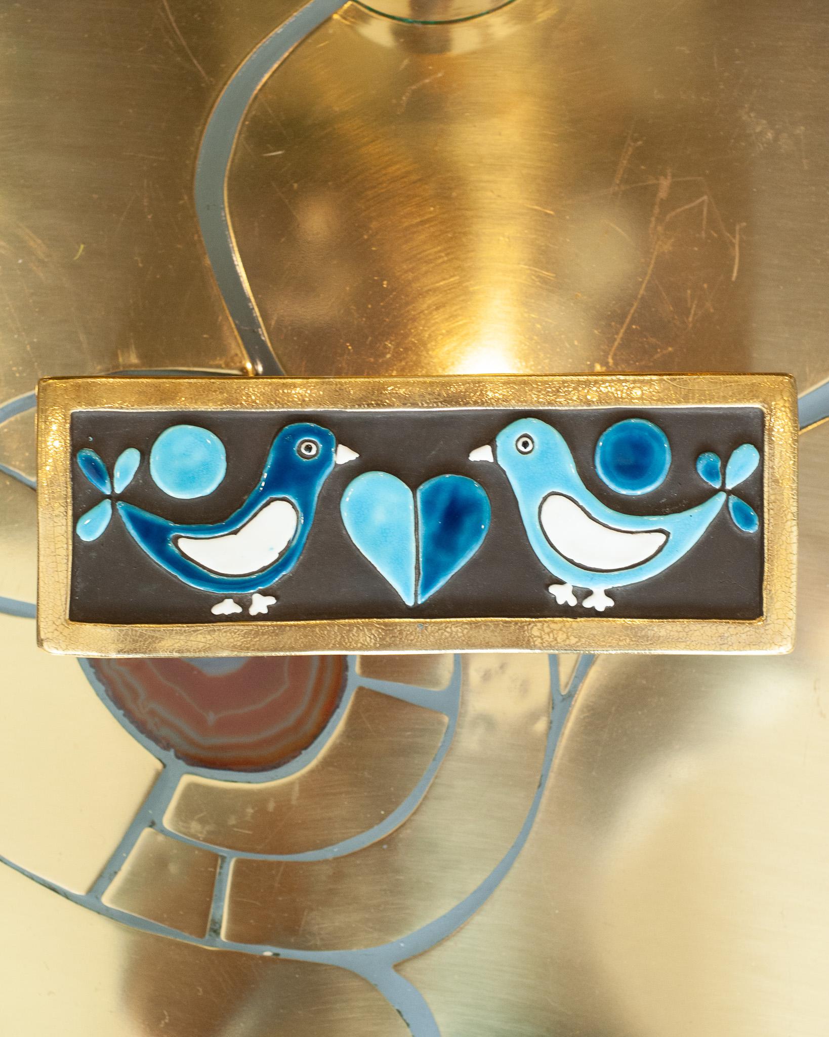 Un'eccezionale scatola in ceramica smaltata di metà secolo con bordo in oro liquido e uccelli bianchi e blu, opera della famosa artista Mithé Espelt. Il coperchio della scatola è in ceramica con una base in legno annerito.
Nata nel 1923, Mithé