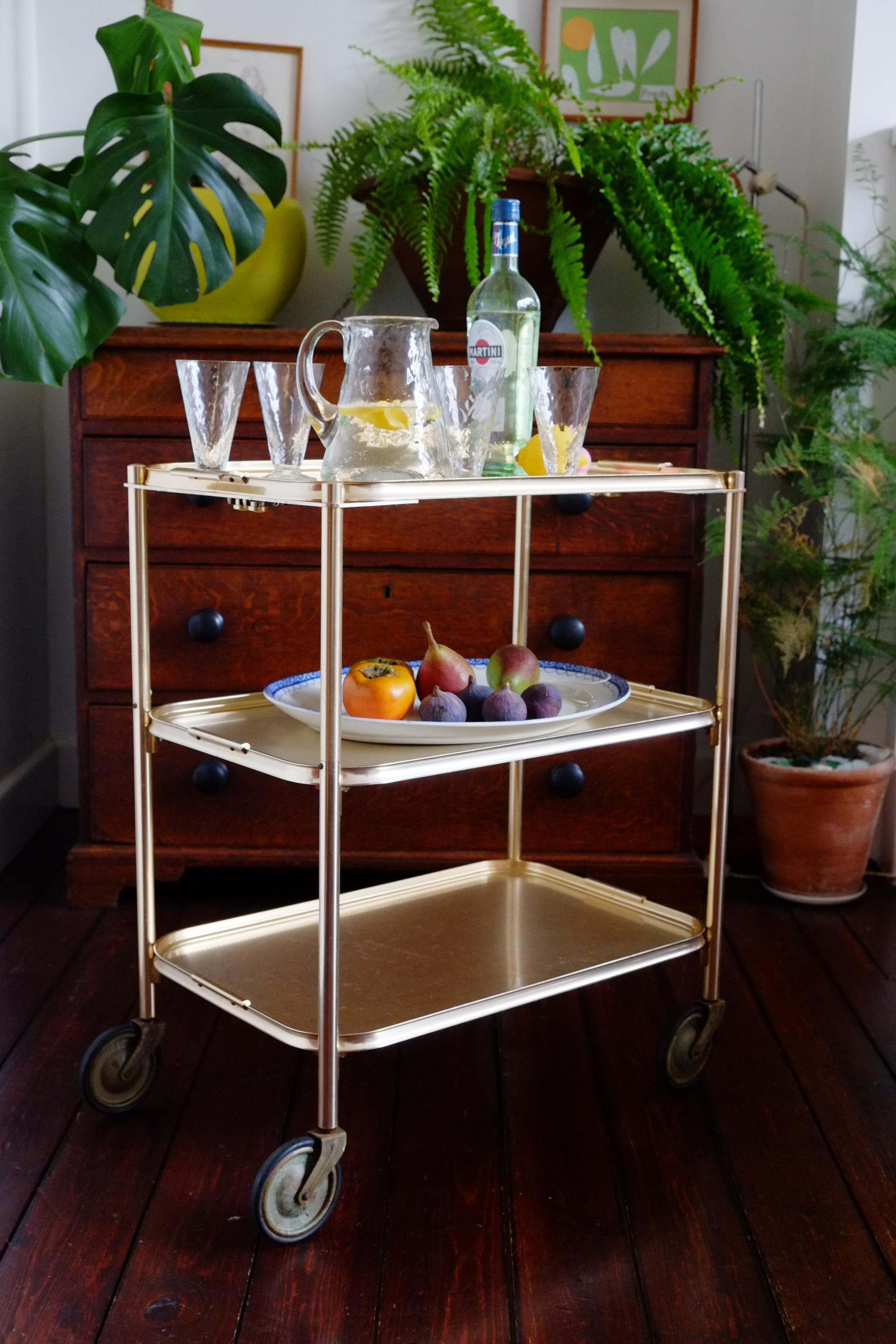 Chariot de bar en or du milieu du siècle dernier Chariot des années 1960. Fabriqué à Manchester, en Angleterre, par Carefree. Ce chariot a une forme classique magnifique avec trois plateaux et de grandes roues. Fabriquée en aluminium avec une