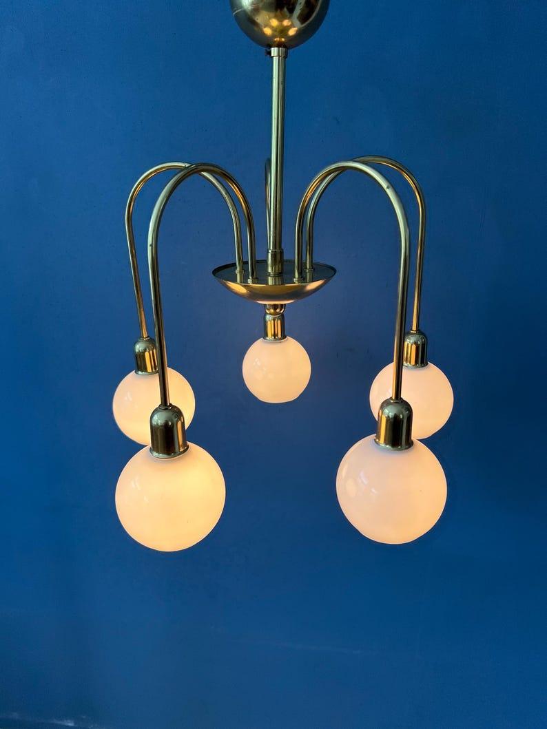 Lampadario di metà secolo in vetro opalino con cinque paralumi in vetro e struttura in ottone dorato. I paralumi sono piccoli e hanno delle aperture nella parte inferiore. La lampada richiede cinque lampadine E14.

Informazioni