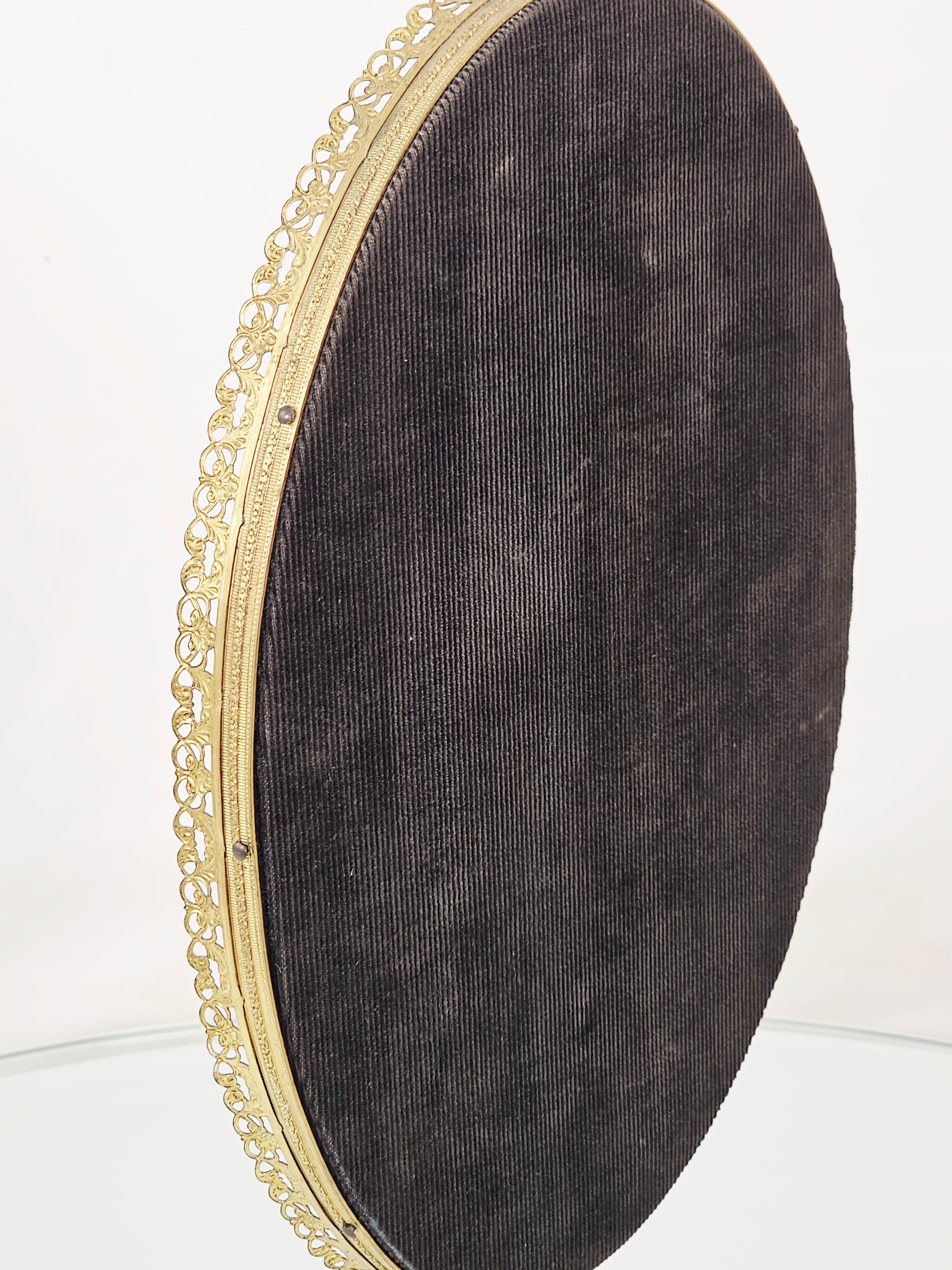 Vintage vanity mirror, ornate details on the base and frame. 
Or tabletop makeup mirror. 
Looks like it belongs in a 50s boudoir. 
Made of cast brass with gold plating, and a glass mirror. 
Mirror is showing age.
Fabric on the back is still in