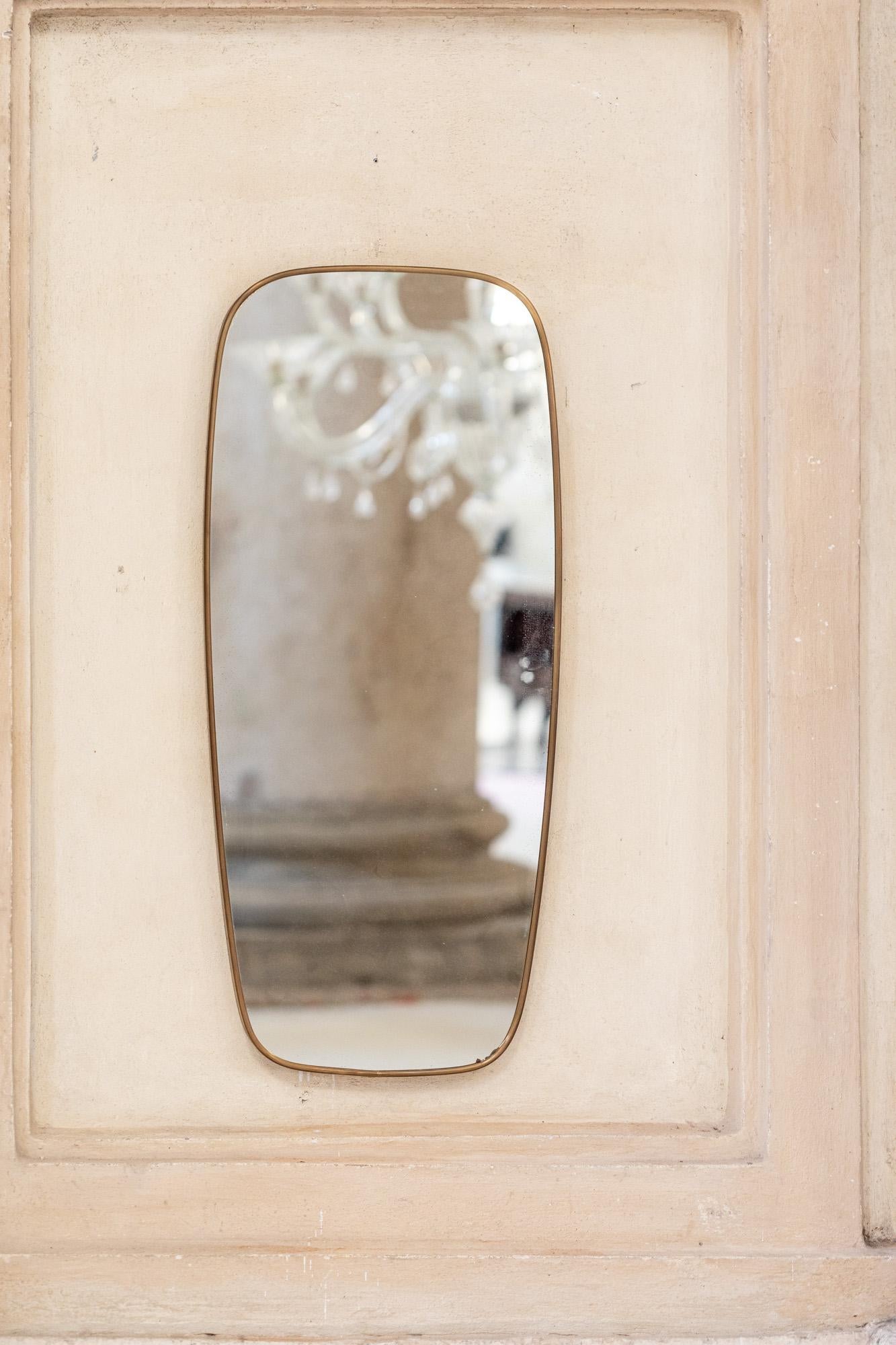 Elegante espejo de pared de latón atribuido a Gio Ponti.
Marco de latón dorado patinado con forma sinuosa y espejo original.