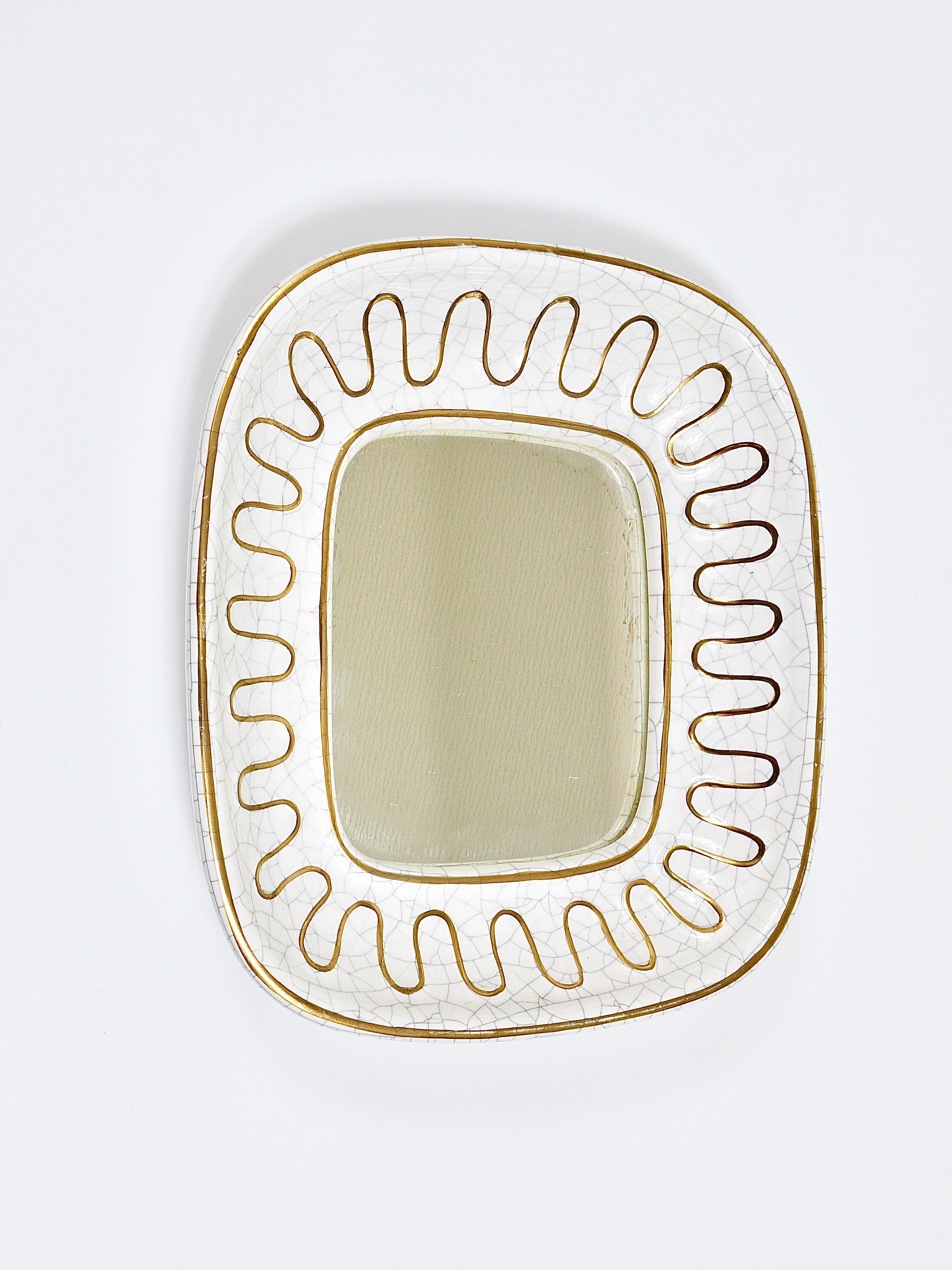 A lovely shaped wall-mounted mirror from the 1950s, manufactured by Gmundner Keramik in Austria. Made of ceramic / pottery with a wonderful white crackled glaze and  decorative golden loops around the frame. In very good condition. The mirror glass