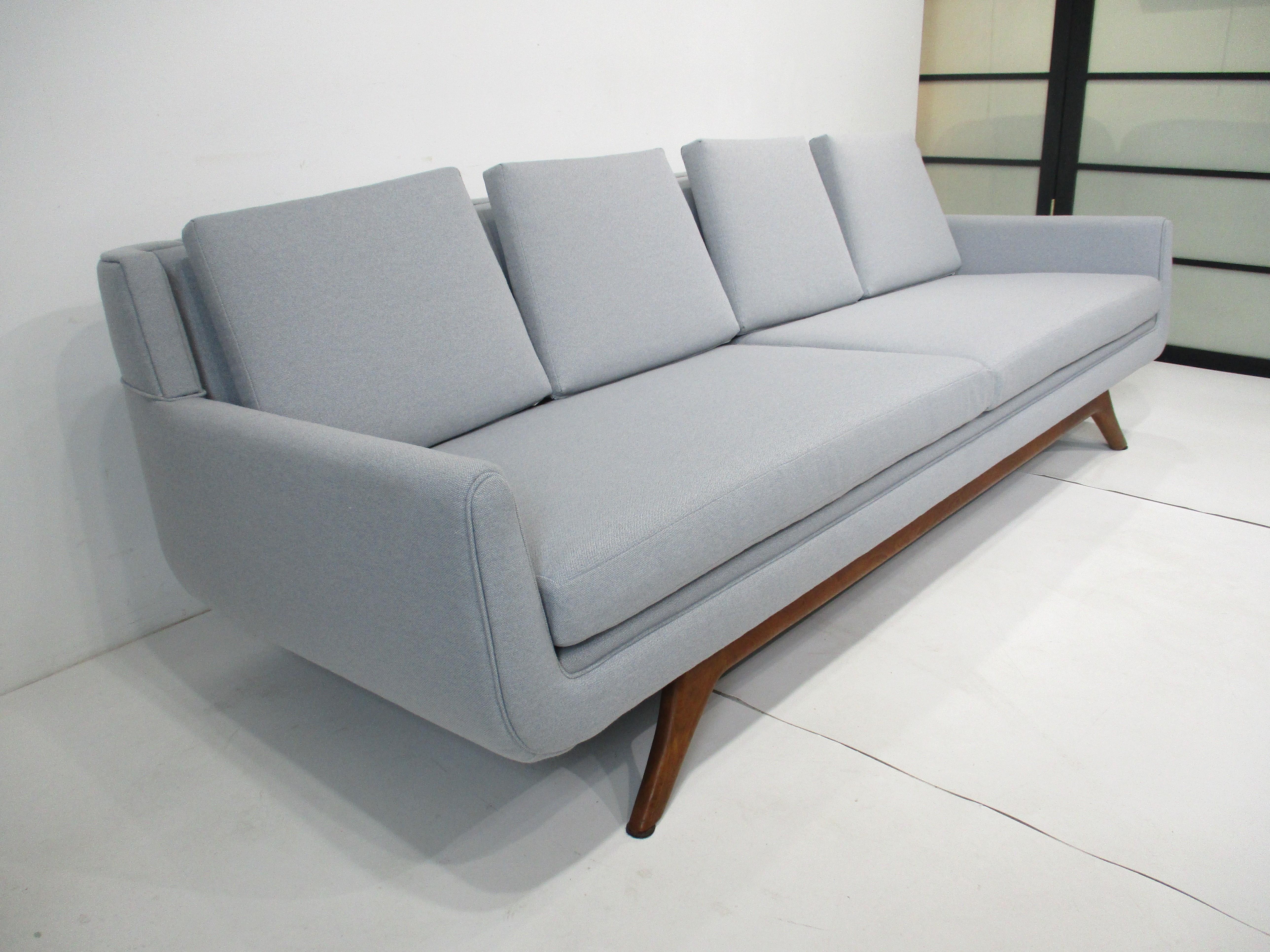 A very well crafted gondola styled sofa with loose bottom and back cushions resting on sculptural walnut legs . This Mid Century sofa is reupholstered in a lighter gray with a slight hint of very light blue in a tight woven contract Knoll fabric .