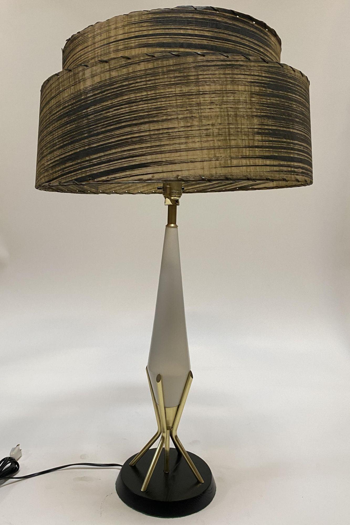 Original Mid Century Googie table lamp featuring a black base connected to 3 brass rods which support tapered lamp neck. 

Included is the whipple stitch fiberglass lamp with modernist pattern along the front. 

Lamp: 24