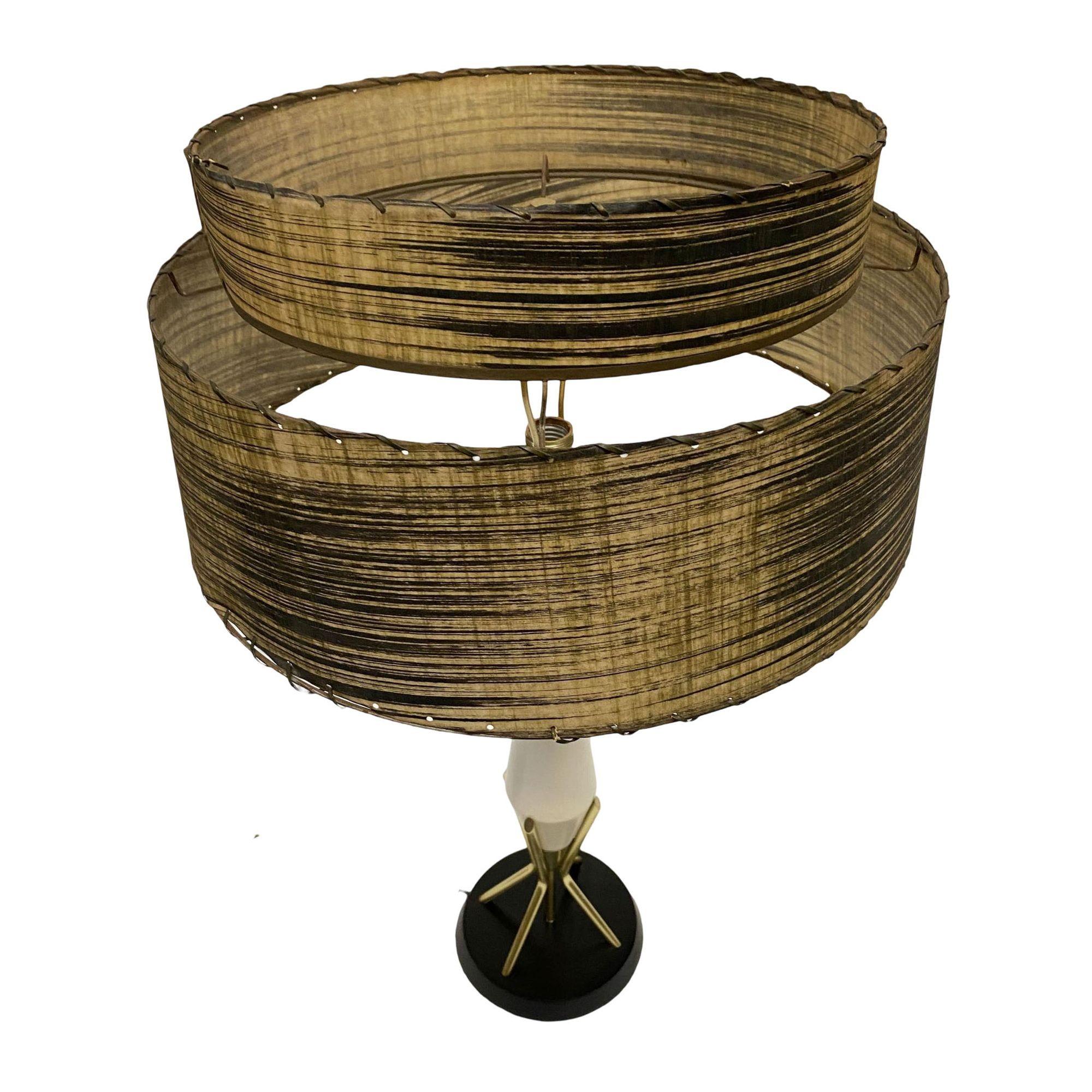 Original Mid Century Googie table lamp featuring a black base connected to 3 brass rods which support tapered lamp neck.

Included is the whipple stitch fiberglass lamp with modernist pattern along the front.

Lamp: 24