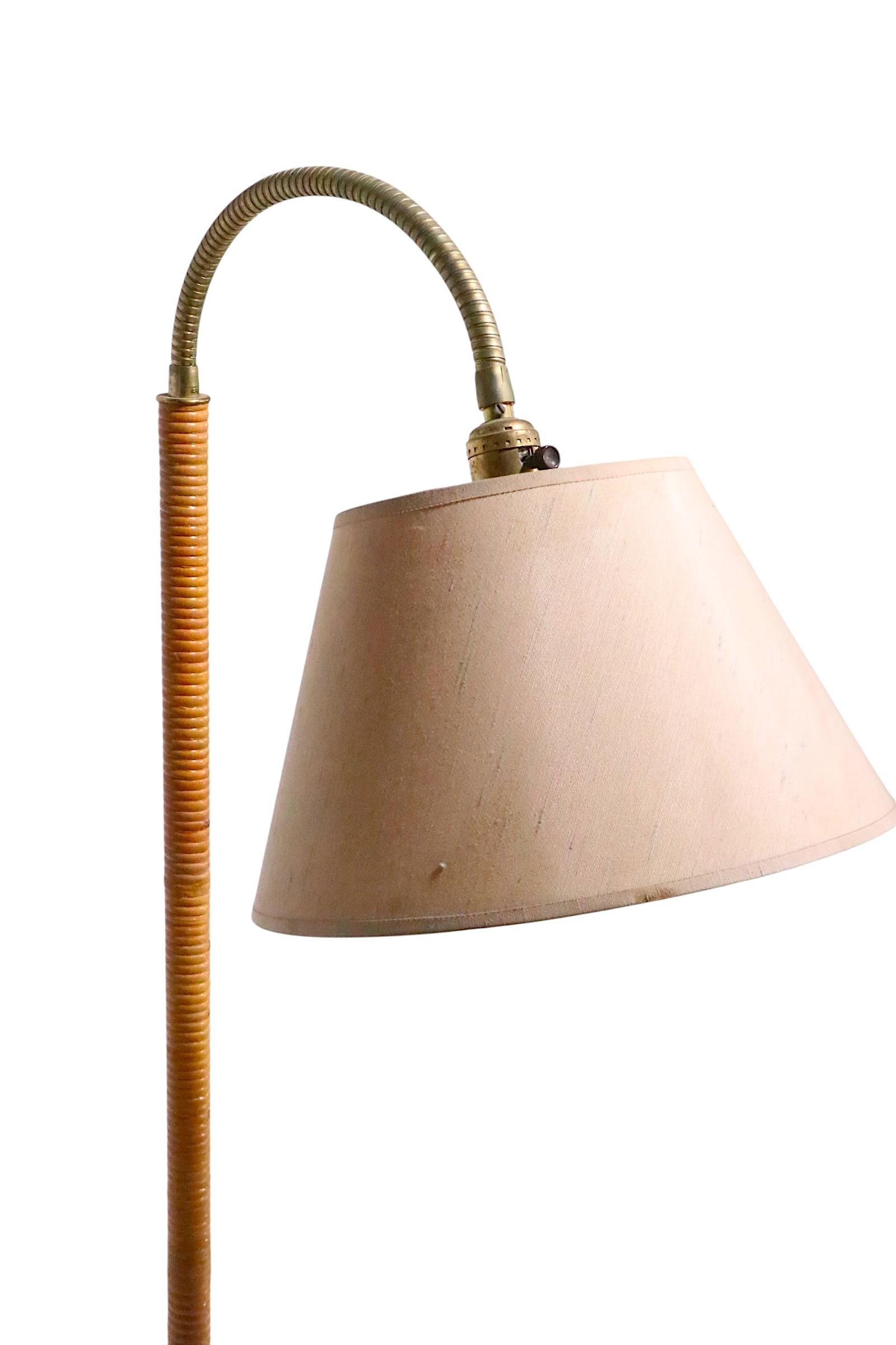Lampadaire Chic Mid Century, Hollywood Regency, Coastal style, ayant un standard vertical central enveloppé de canne, monté sur une base de couleur laiton, avec un bras flexible en métal, et un abat-jour d'origine. Exécuté à la manière de Tynell,