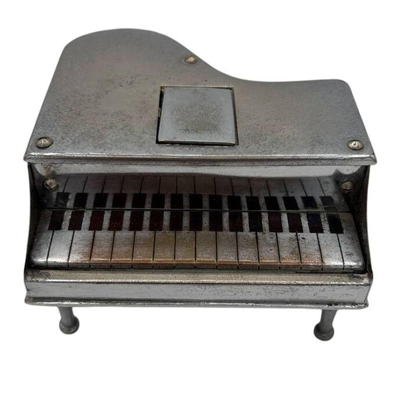 This vintage figural chromed steel grand piano table lighter, made in Japan, combines playful design with clever functionality. Shaped like a miniature grand piano, it features intricate details, including a realistic lid, legs, and keys. The