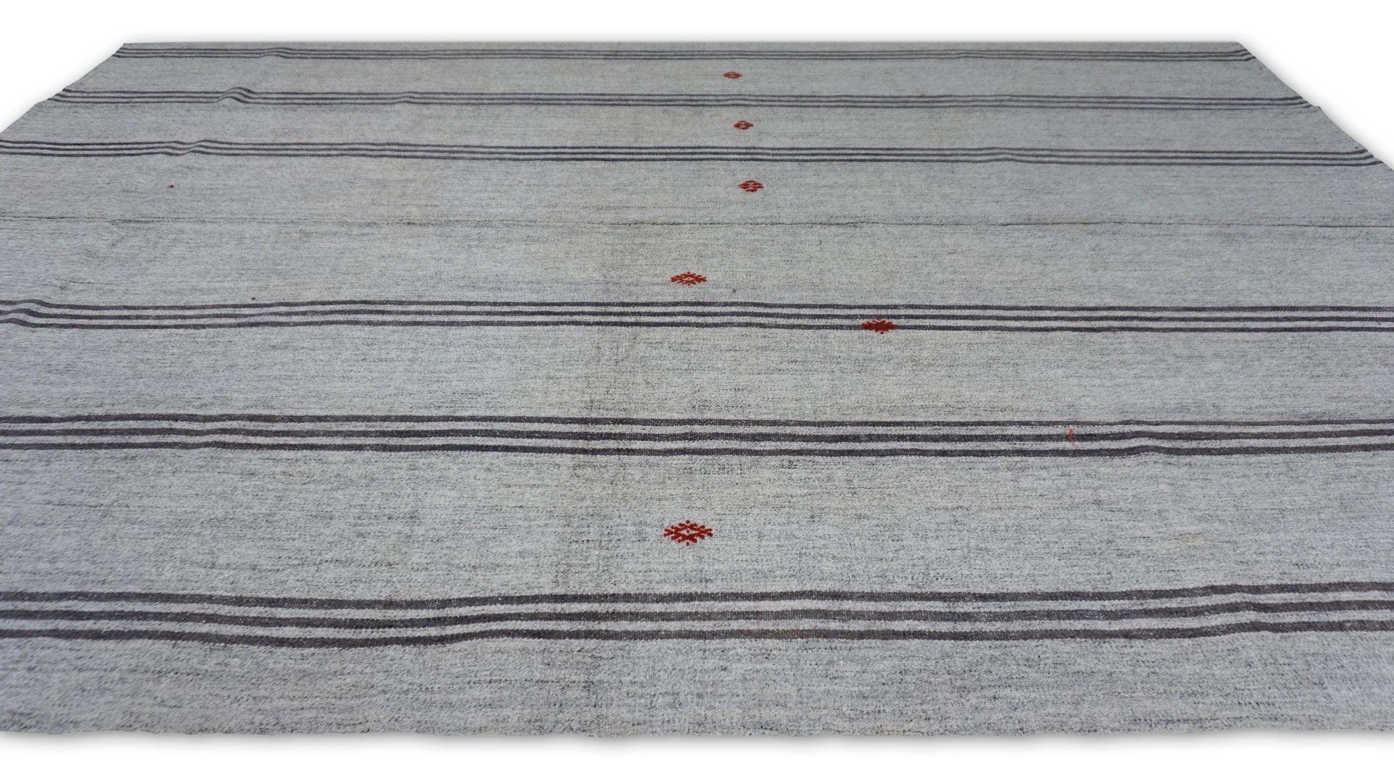 Dieser Vintage-Kelim verkörpert eine raffinierte, minimalistische Ästhetik mit eleganten vertikalen Streifen in sanftem Grau, Greige und Elfenbein. Das zurückhaltende Design wird durch zarte rote Stammesmotive subtil aufgewertet, die ein Element der