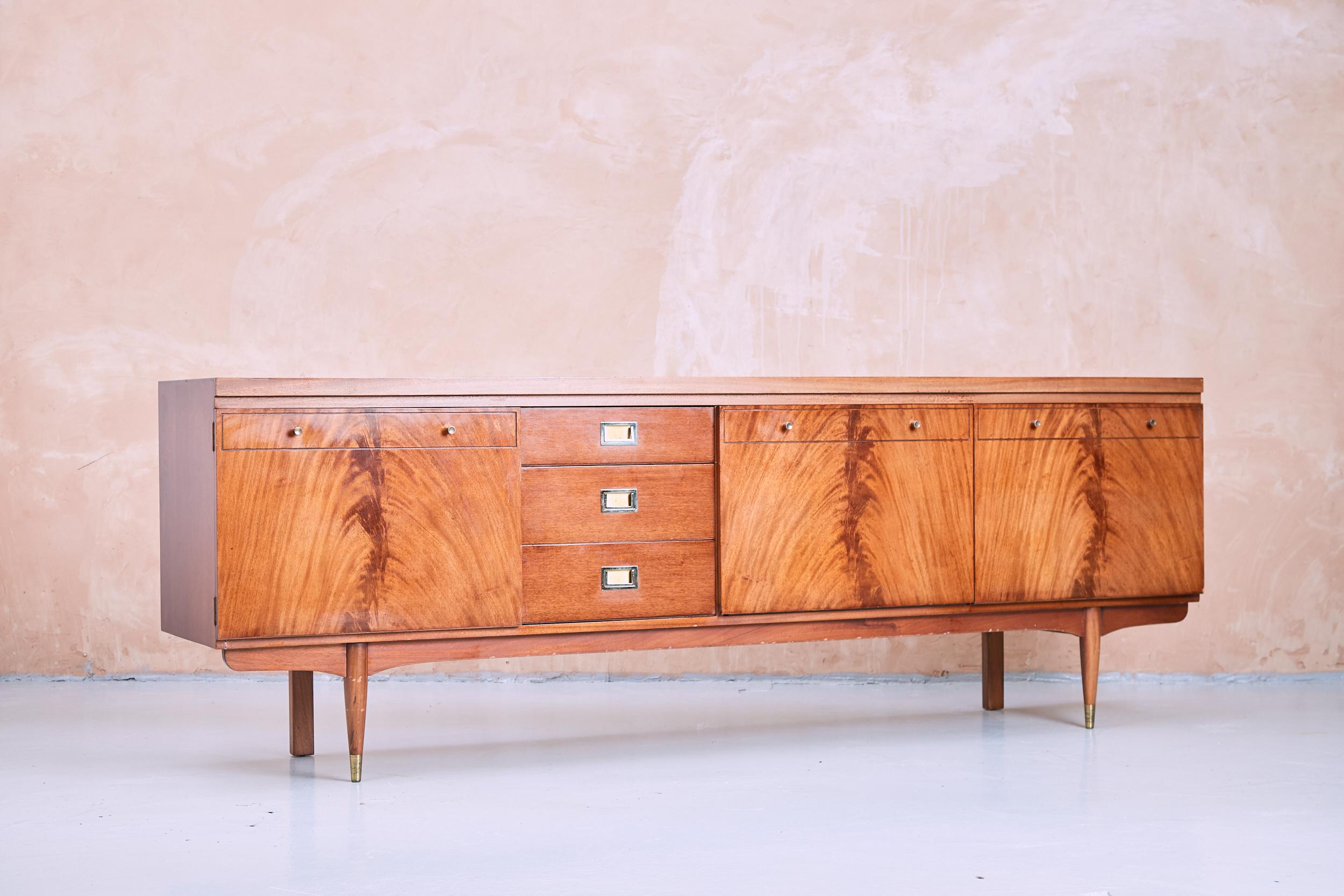 Stylish midcentury sideboard or server. Manufactured by Greaves & Thomas who were inspired by Danish furniture design in the mid-20th century. Handsome flame mahogany veneer exterior with a dark finish. Ample storage space with cabinets and dovetail