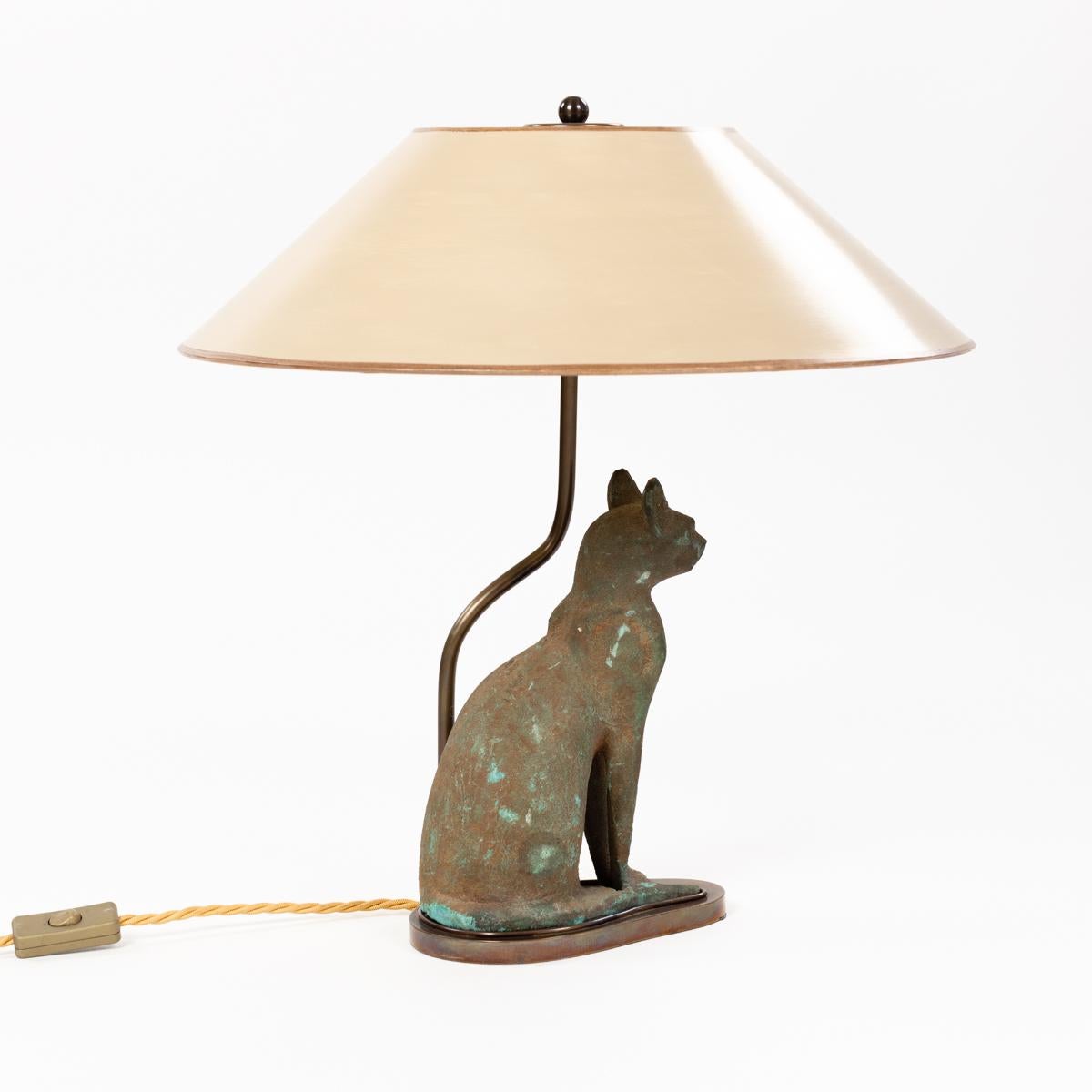 Lampe de table Bastet Cat God en fer patiné du milieu du siècle dernier 
L'objet lourd, en fonte, est légèrement surdimensionné dans ses contours. 
L'animal est assis dans une posture droite, la queue est placée en avant et les oreilles sont