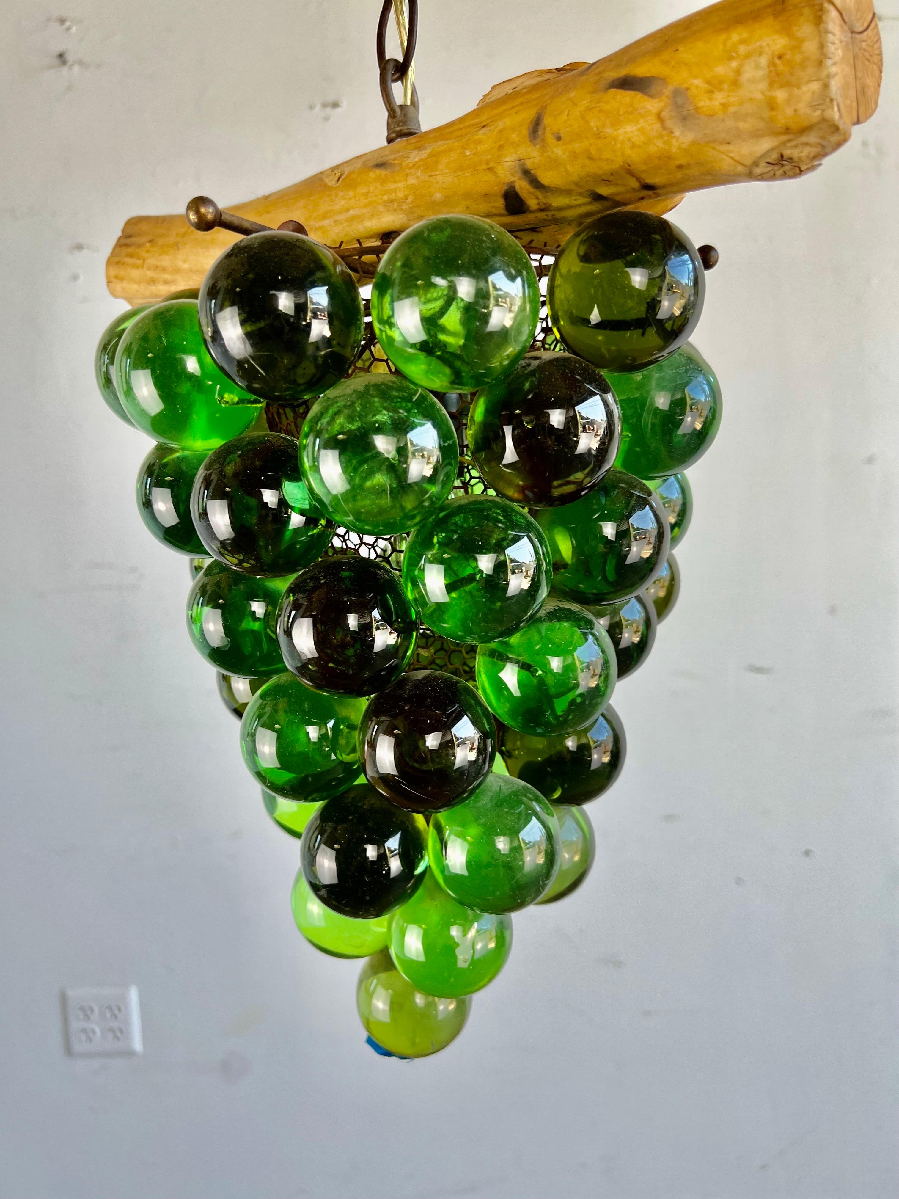 A light fixture made from a bunch of green acrylic grapes hanging from a piece of wood. The fixture is in newly wired and in working condition.
