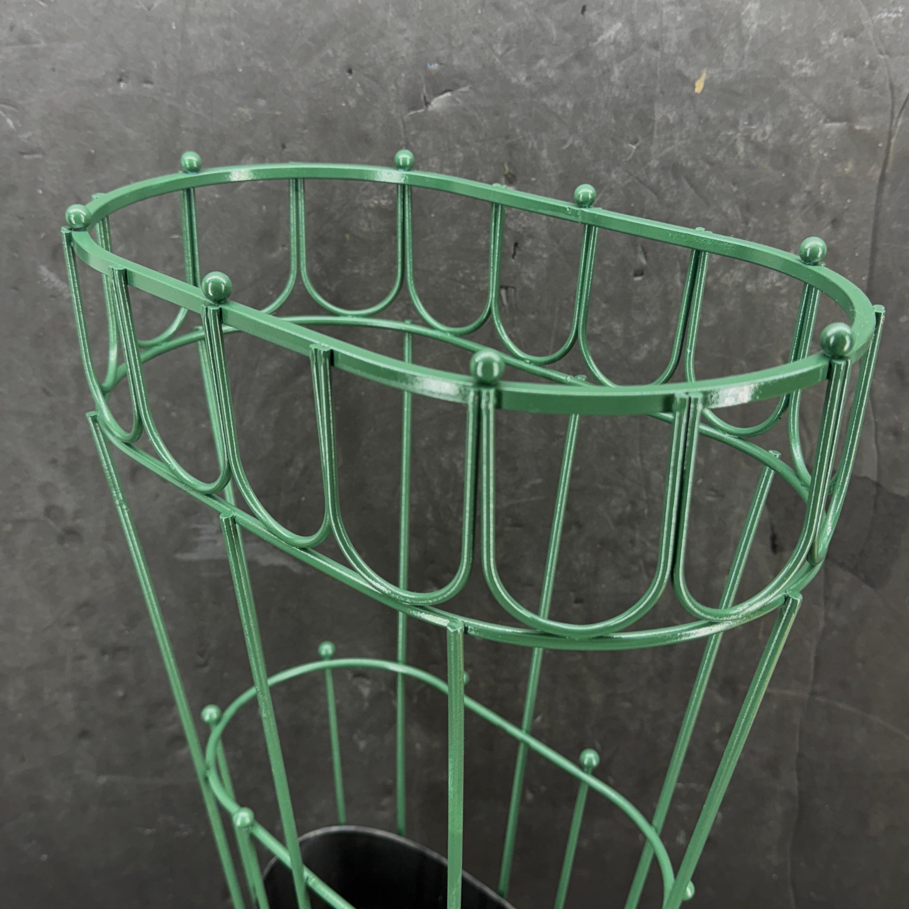 Ce porte-parapluie est peint dans une couleur verte classique. Ce support est très polyvalent et peut être utilisé aussi bien près de la porte d'entrée que dans une salle de séjour. Nous voyons également ce stand dans un environnement de vente au