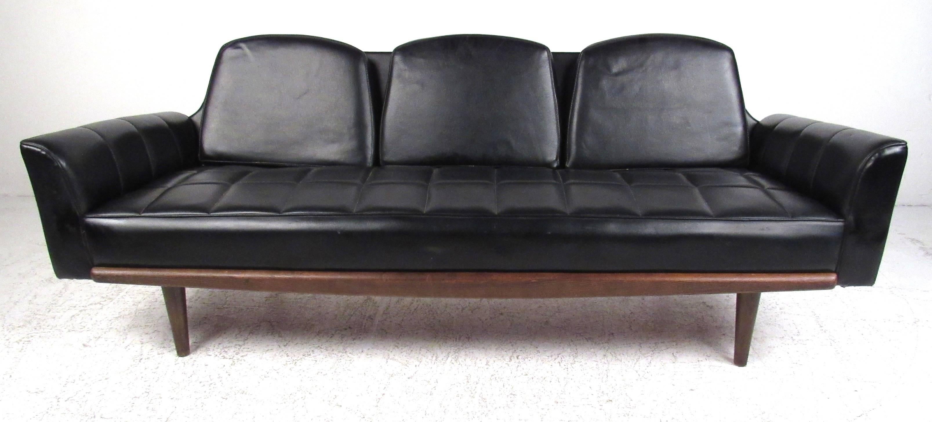 Classic midcentury black vinyl sofa featuring a grid tufted pattern across the seats and arms. Oak trim
compliments the base with tapered wood legs in front and sculptural legs in the back. The lower profile makes
it perfect for a smaller modern