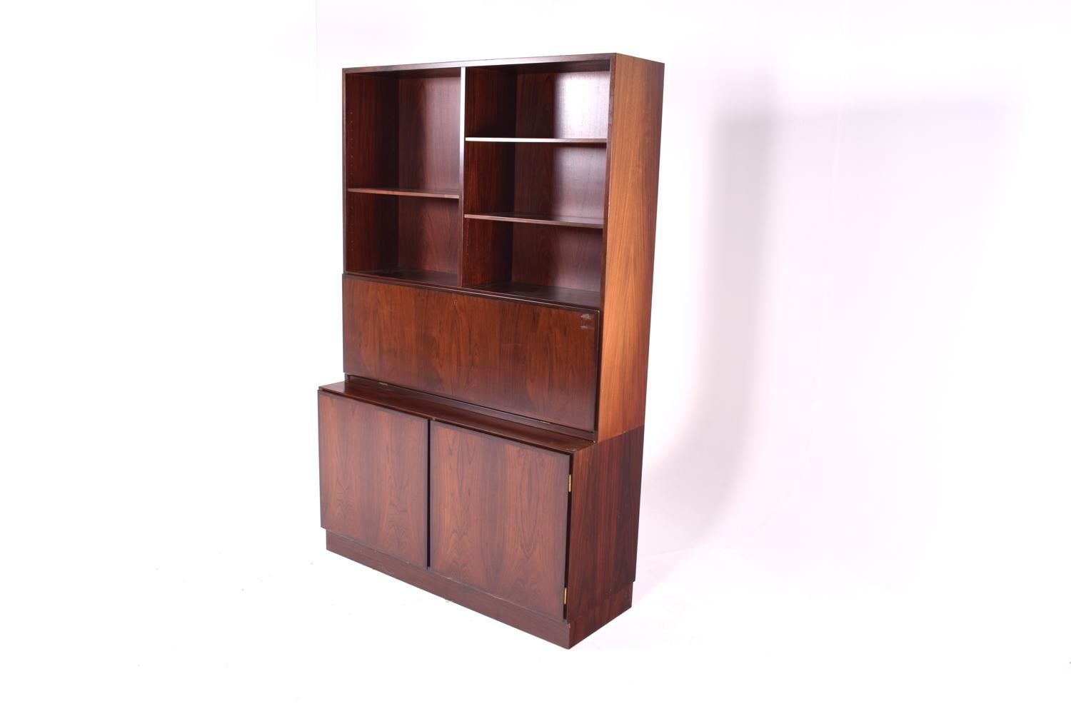 Rosewood bookcase with 6 bevel edge shelves. Desk compartment fitted with interior drawers. Platform base. Elegant and exotic rosewood veneer in a geometric clean design by Gunni Omann.