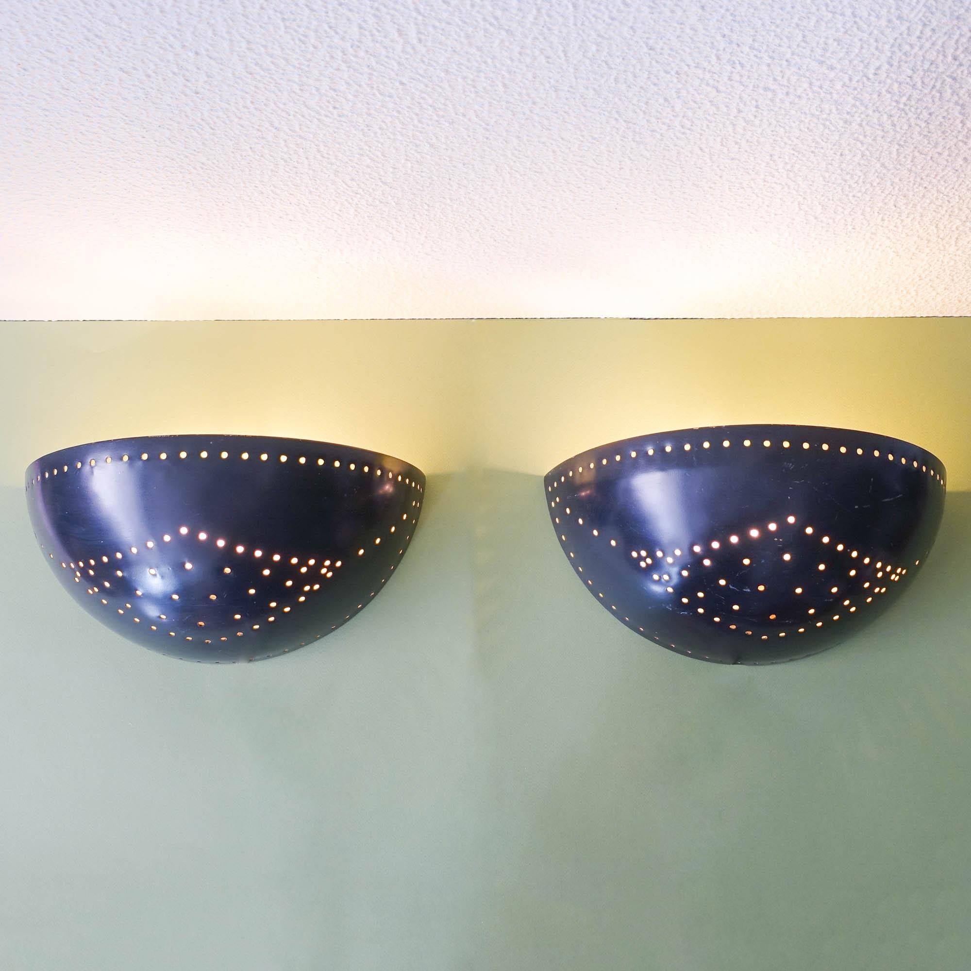 This pair of wall sconces was designed and produced in Italy, during the 1950's. They are in the shape of half moon, made of solid brass. They feature a black lacquered brass which is perforated, giving these sconces when lit, a beautiful light