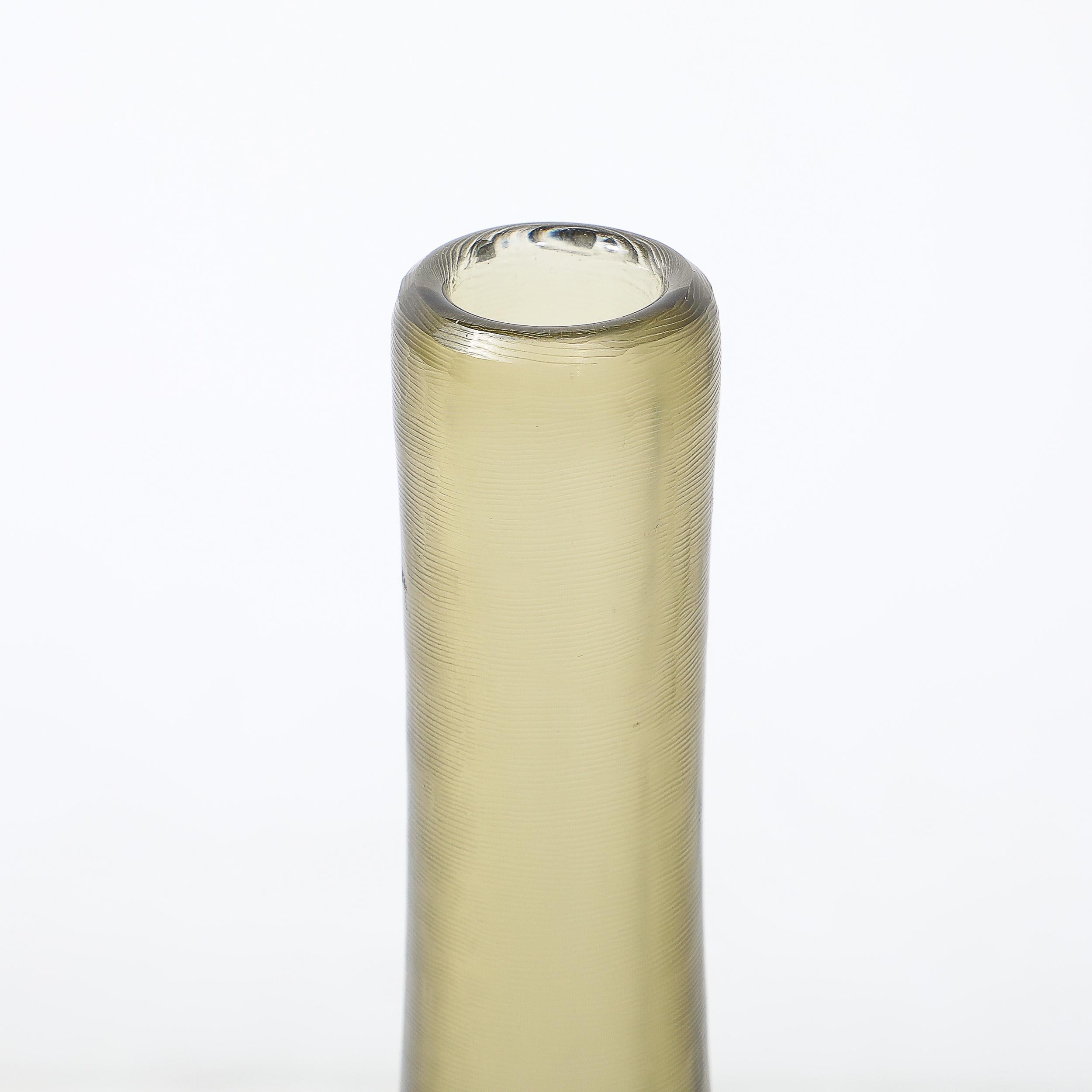 This timeless Mid-Century Modernist vase, crafted in Italy circa 1960, exemplifies the mastery of Murano glass artisans. Hand-blown in a rich sap green hue, the vase exudes an understated elegance and sophistication. The fine textural reeded