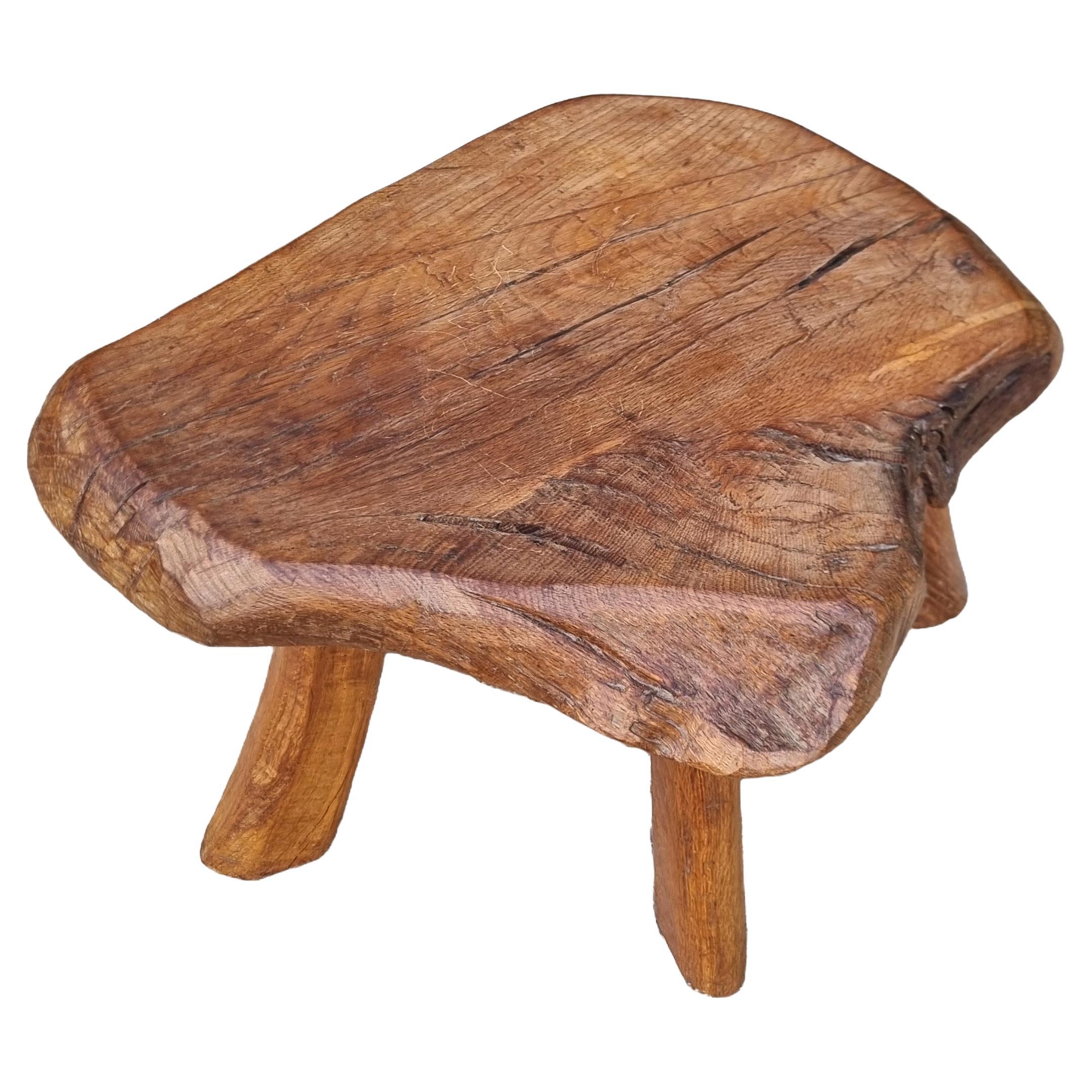 Characterful mid-century stool crafted from a single slab of solid oak with a beautiful live-edge top and four slightly splayed, hand-shaped legs. The irregular seat shows rich grain, tool marks and age checks that give the piece a warm, wabi-sabi