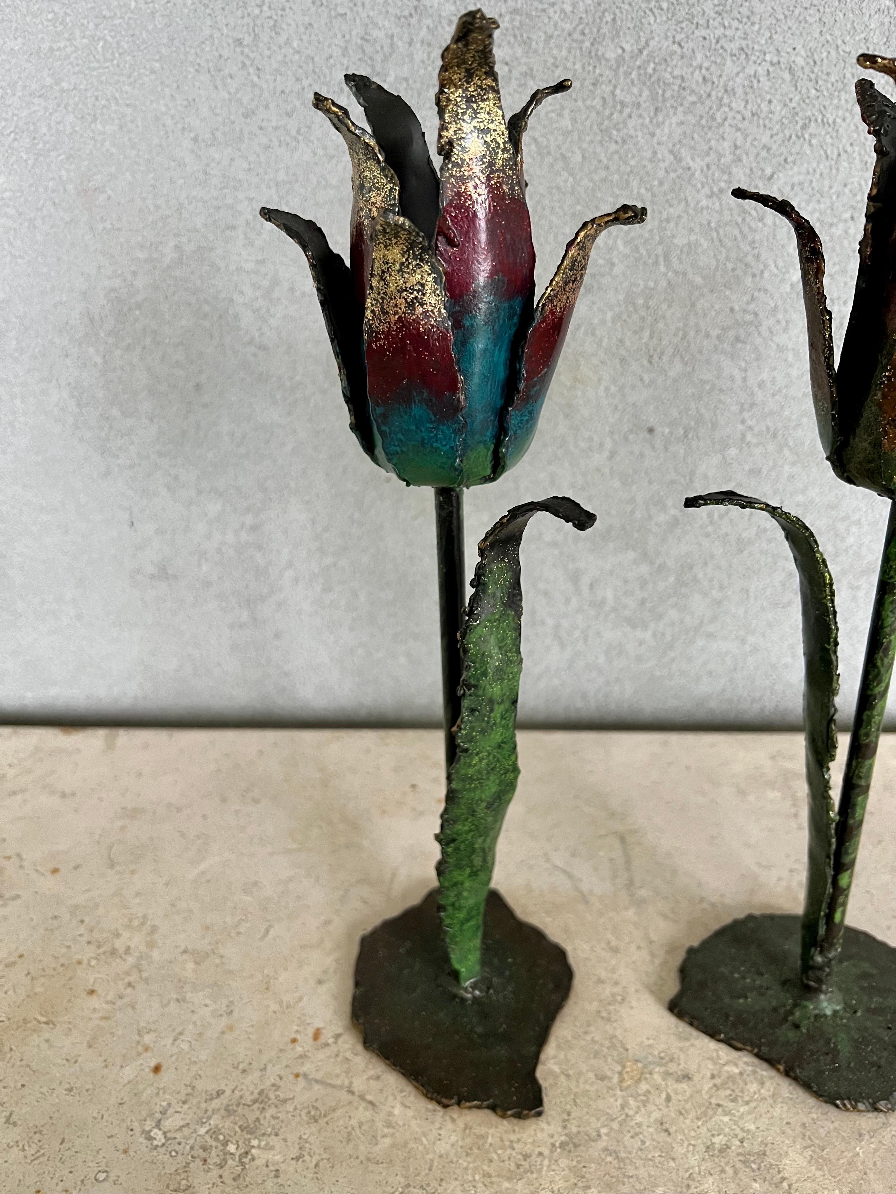 Beautifully crafted pair of hand-made iron tulip.
Candlesticks, hand painted with a shade of colors.
One of them has shades of oranges the other shades of blues, greens and puebles.
The irregular 4”x5” bases are also made of iron, both