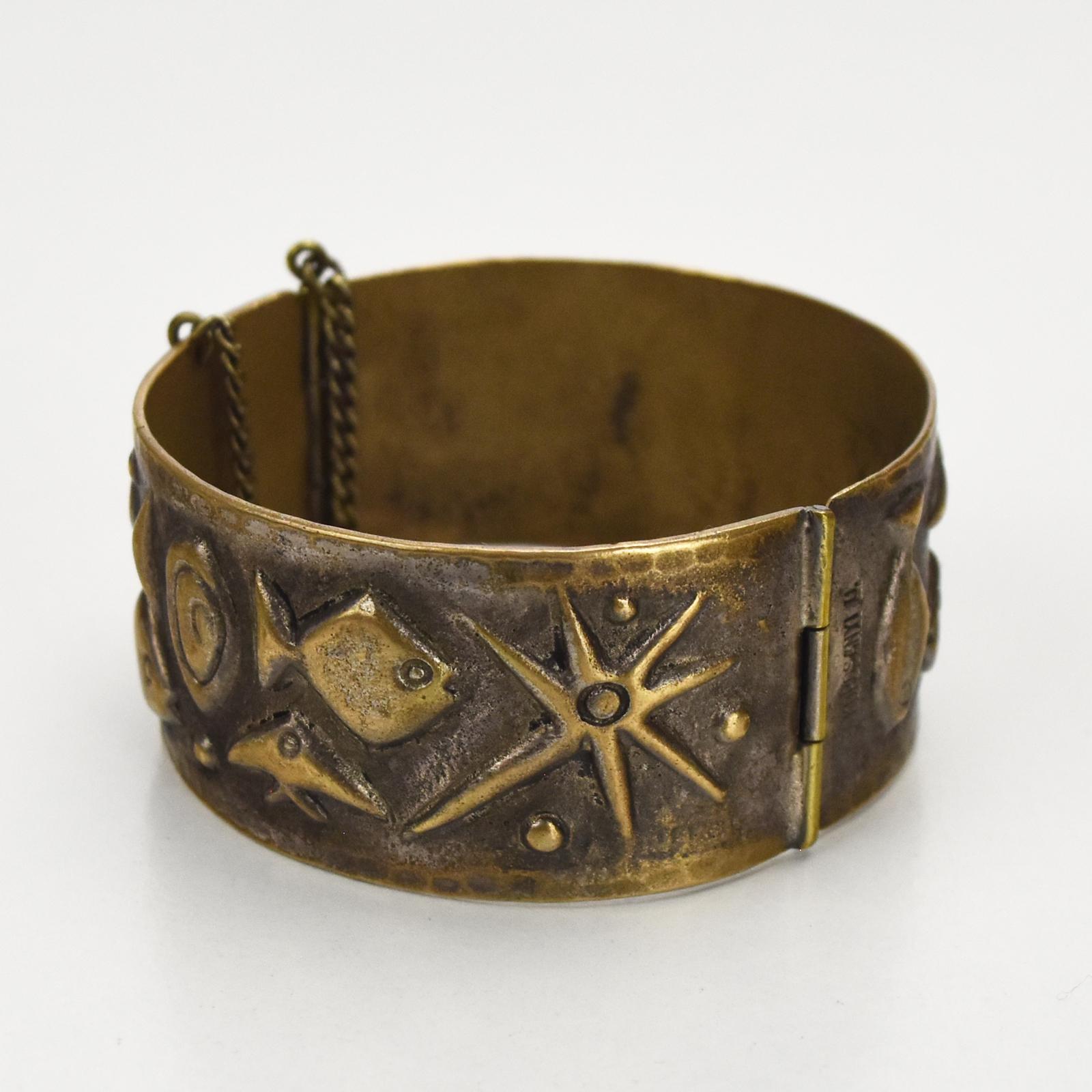 This beautiful handcrafted bronze hinged bangle or bracelet showcases a striking mid-century modernist fish pattern, signed by the artist Korosanyi. The detailed embossing of stylized fish motifs and star-like forms lends a unique, artistic flair,