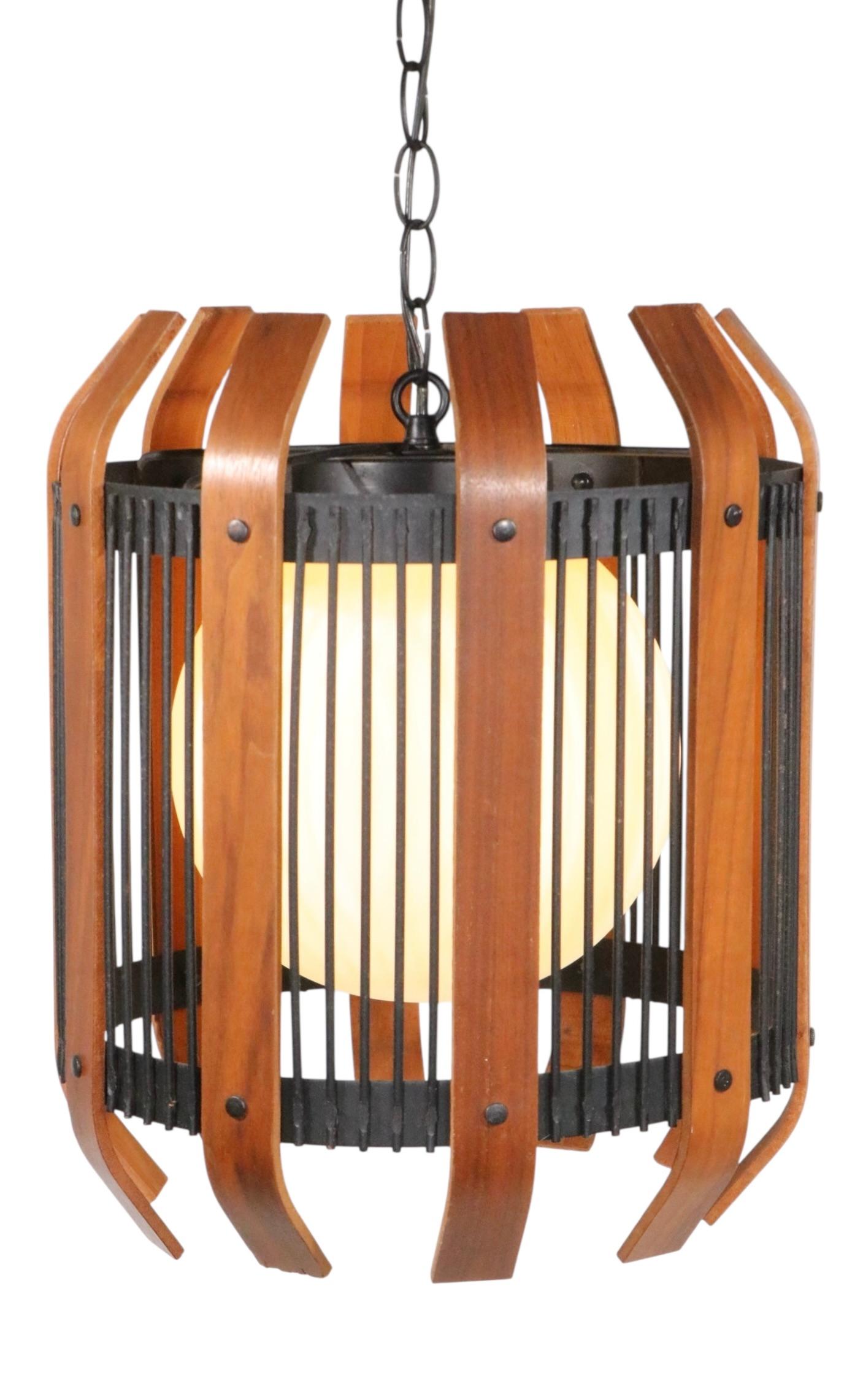 Classico apparecchio architettonico a sospensione di metà secolo in ferro battuto, legno e vetro, realizzato negli Stati Uniti, circa negli anni '50/'60. L'apparecchio è dotato di  una struttura simile a una gabbia in ferro battuto composta da aste