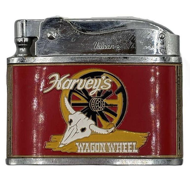 Encendedor de esmalte rojo de los años 50 con calavera de toro y rueda de carreta del Harvey's Wagon Wheel Casino de Lake Tahoe. Este encendedor Harveys Casino Wagon Wheel presenta un atrevido acabado esmaltado en rojo con un distintivo detalle de