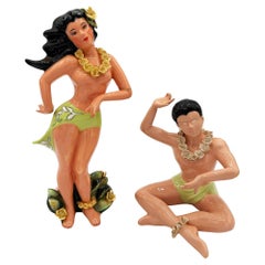 Pareja de estatuillas de cerámica de mediados de siglo, pintadas a mano, con motivos hawaianos: una chica haciendo hula y un surfista