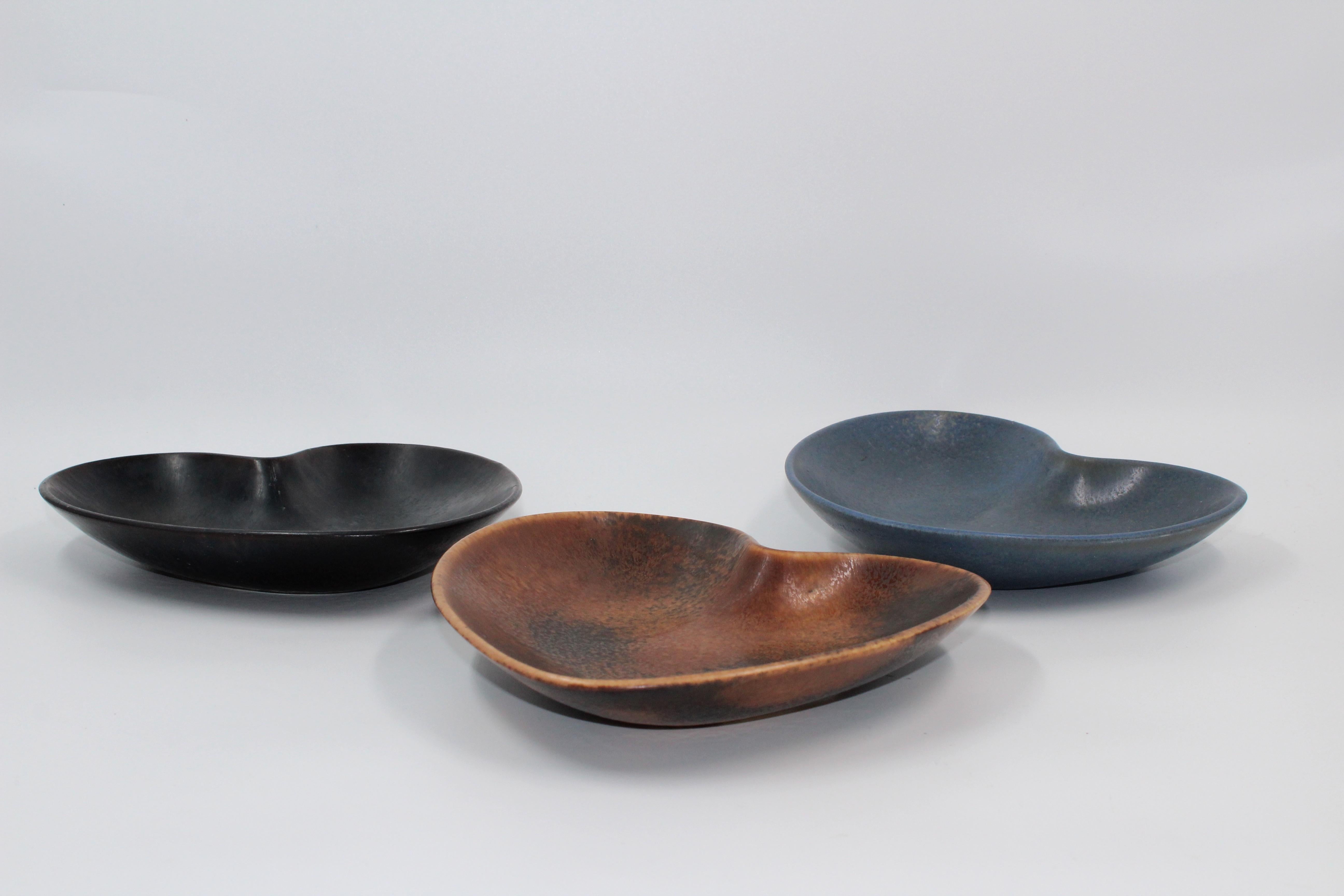 A set of three equally sized heart-shaped ceramic bowls with different glazes designed by Gunnar Nylund. The bowls is in good vintage condition and shows minor signs of usage consistent with age. No damages.