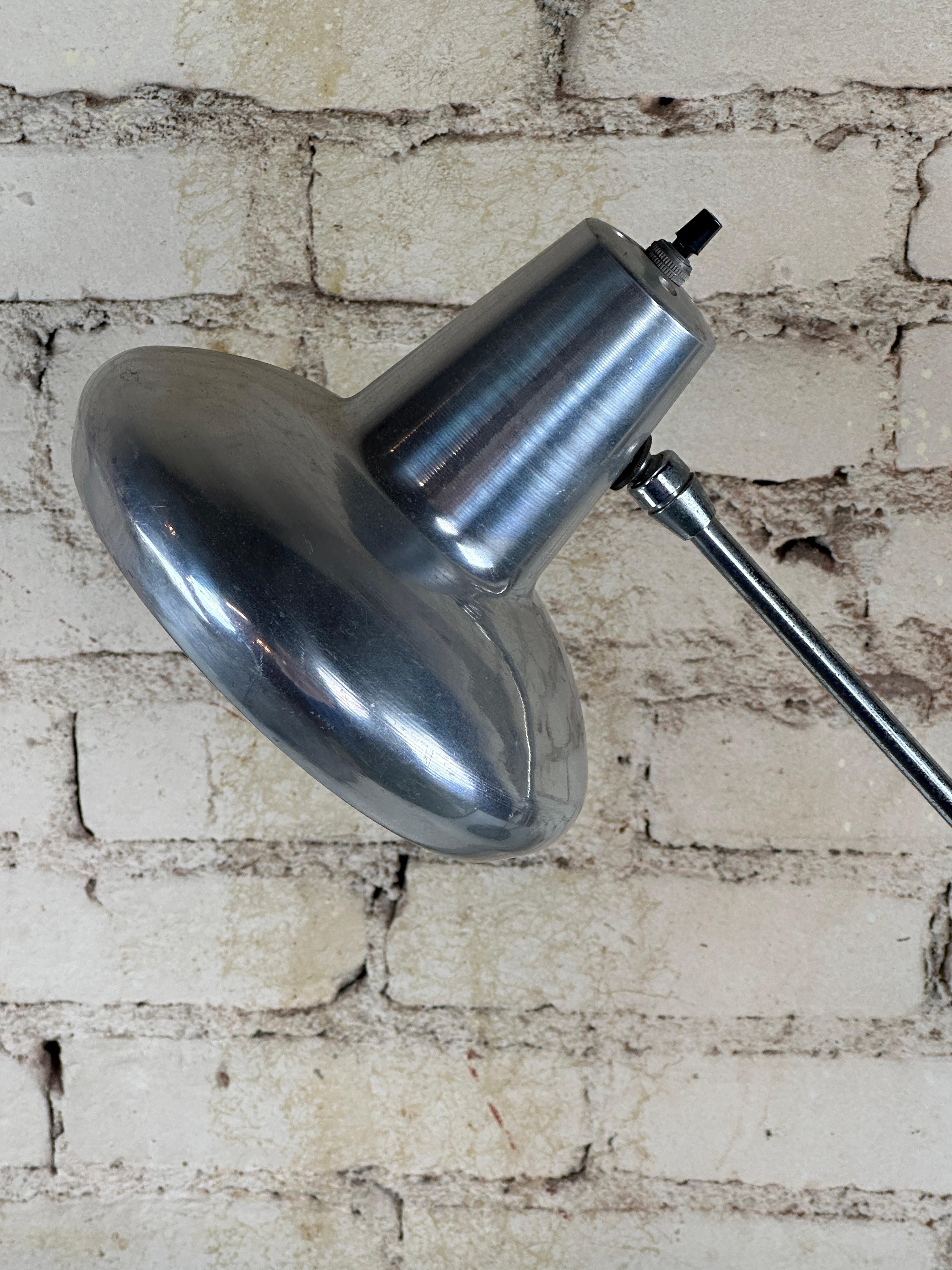 Cette lampe d'atelier du milieu du siècle présente un corps en métal émaillé noir et des accents chromés. 

Sa structure réglable en hauteur permet des options d'éclairage polyvalentes, tandis que l'abat-jour inclinable offre un éclairage ciblé, ce