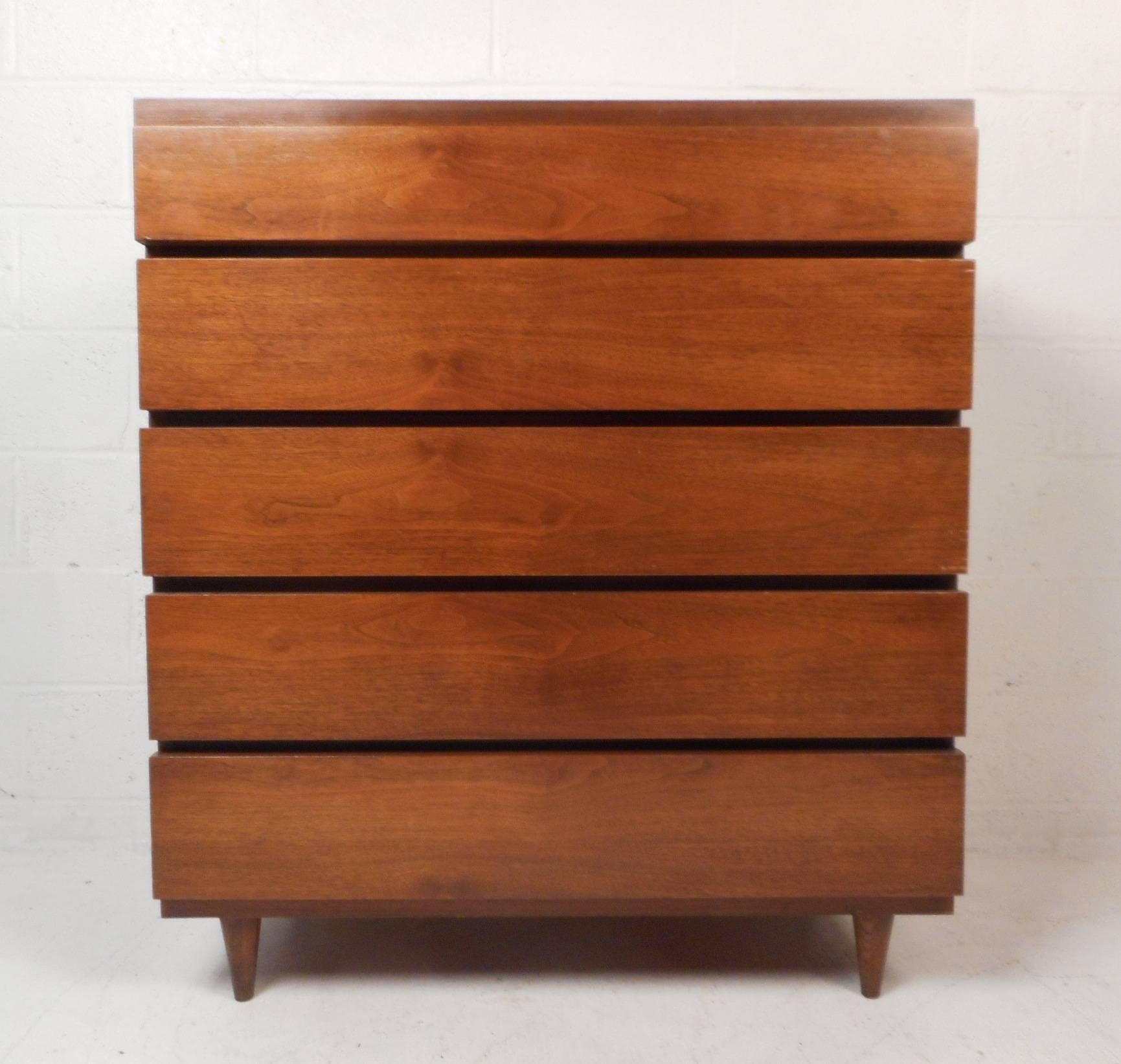 This beautiful vintage modern highboy features five enormous drawers ensuring plenty of space for storage. This well constructed American case piece has sturdy tapered legs and elegant dark walnut wood grain throughout. Very clean piece. The perfect