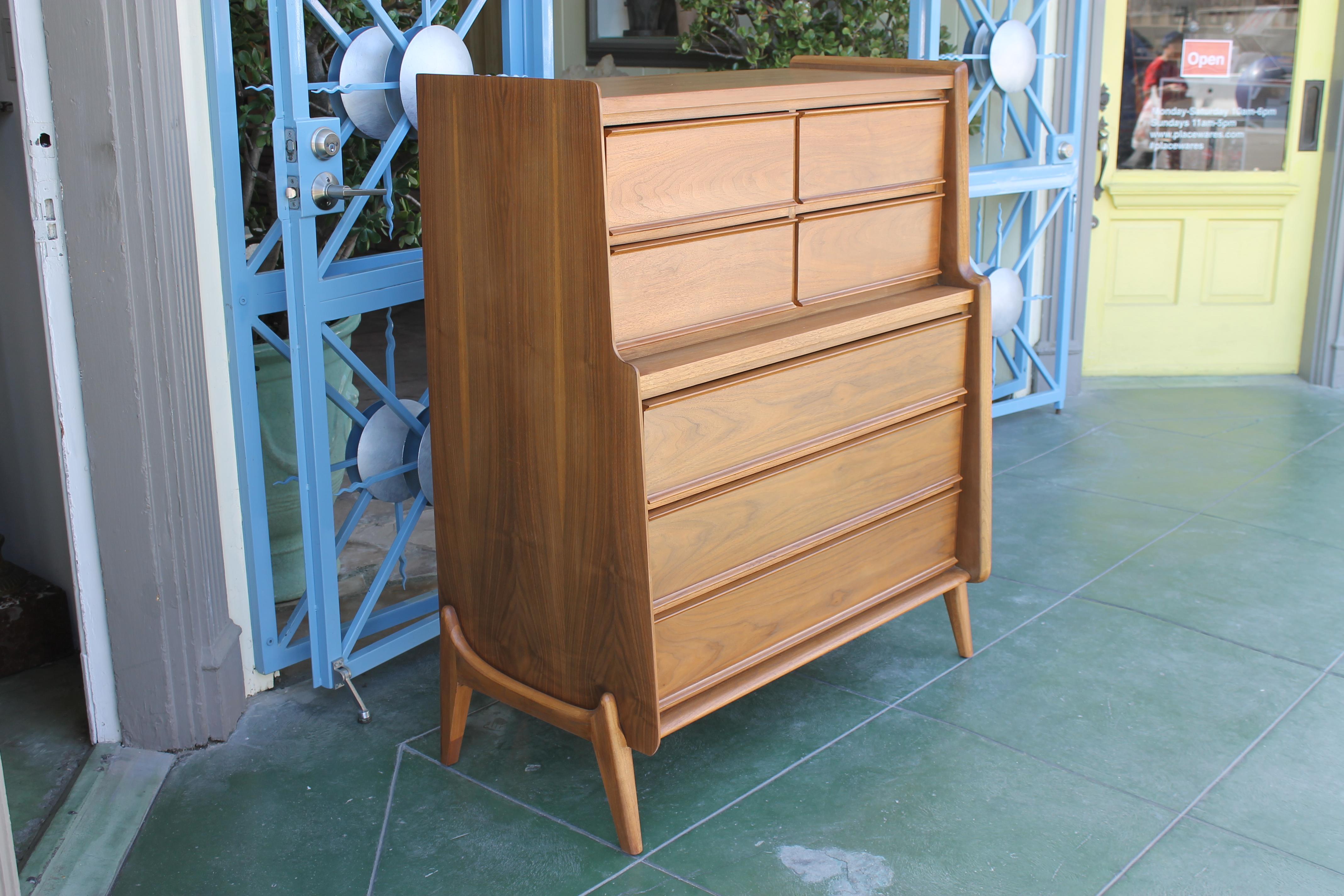 This striking Mid-Century Modern highboy dresser by United Furniture features seven spacious drawers with blind pulls, a sculptural base reminiscent of Kagan and Pearsall, and a modern multi-tiered profile. Four small drawers are on the upper level.
