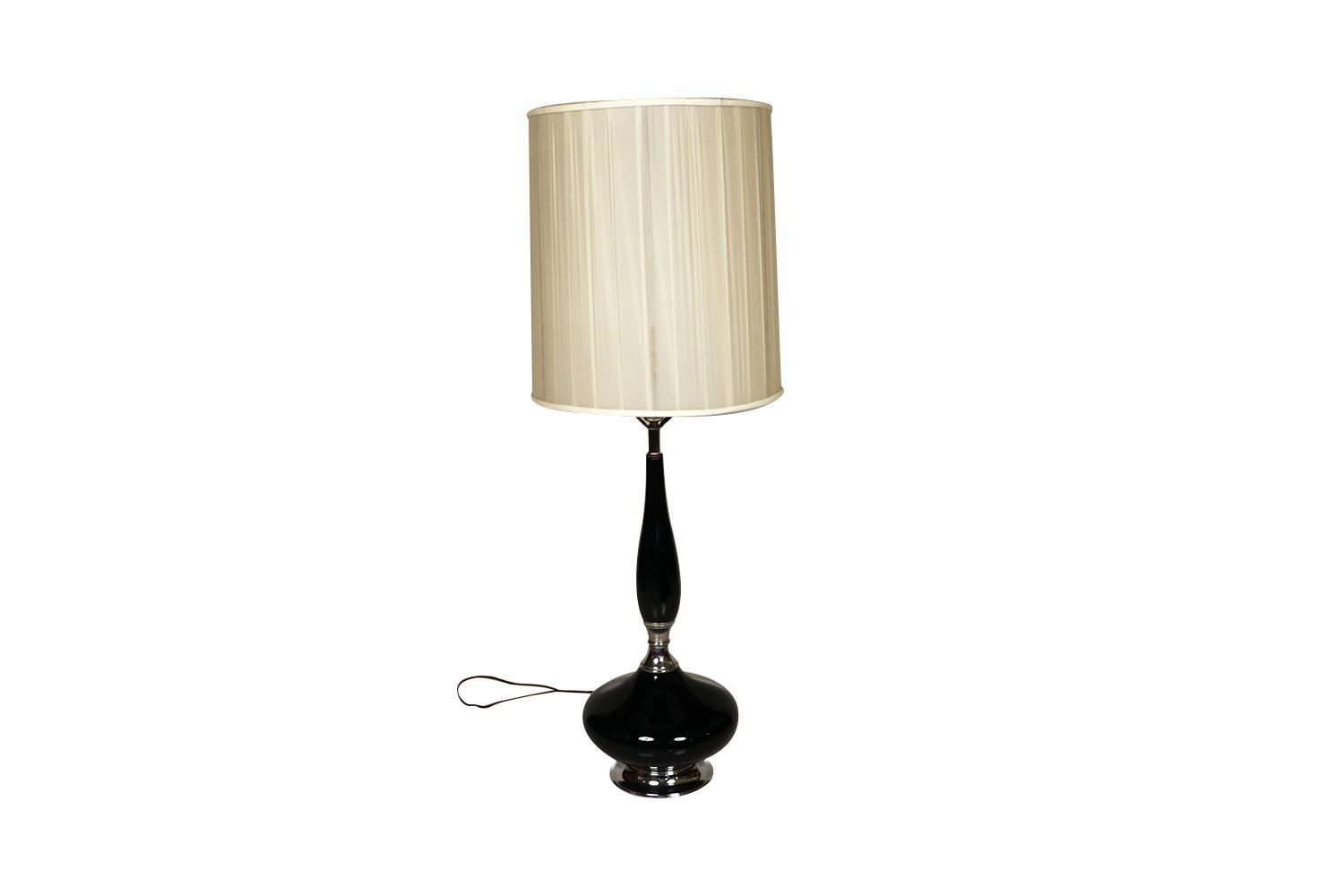 This is a stunning and very sought after midcentury, Hollywood Regency, ceramic table lamp with an elongated neck, over bulbous form, raised on a chrome base, finished off with this beautiful drum lampshade included, featuring a vibrant shiny black