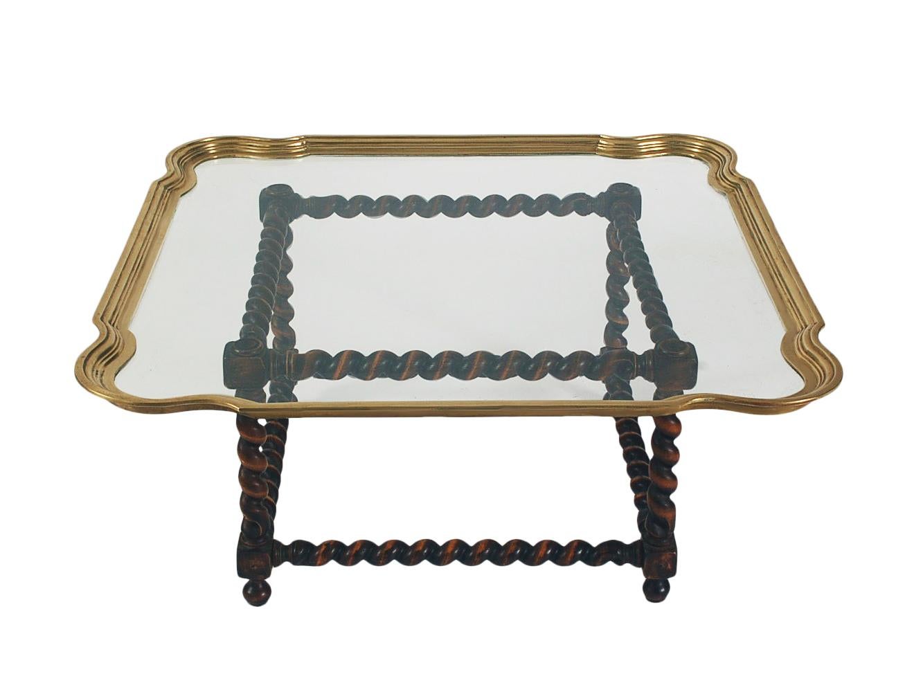 Table basse classique de style transitionnel, datant des années 1970. Elle se compose d'une base épaisse en bois massif et d'un plateau en verre transparent et en laiton.