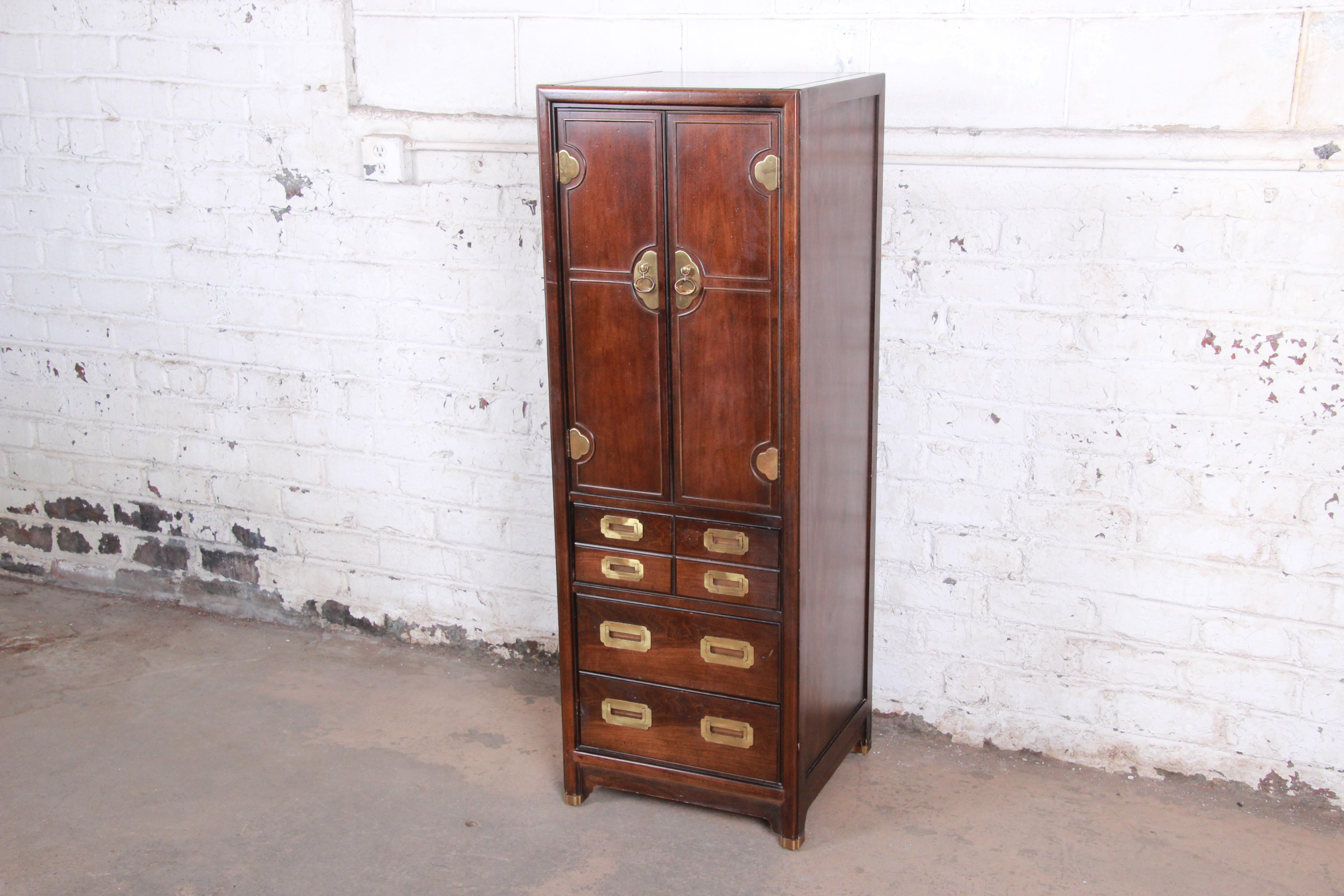 A beautiful midcentury Hollywood Regency Campaign style lingerie chest by Hickory. The chest features gorgeous dark teak wood grain and original brass hardware. It offers good storage, with a single dovetailed drawer and shelf behind two doors and
