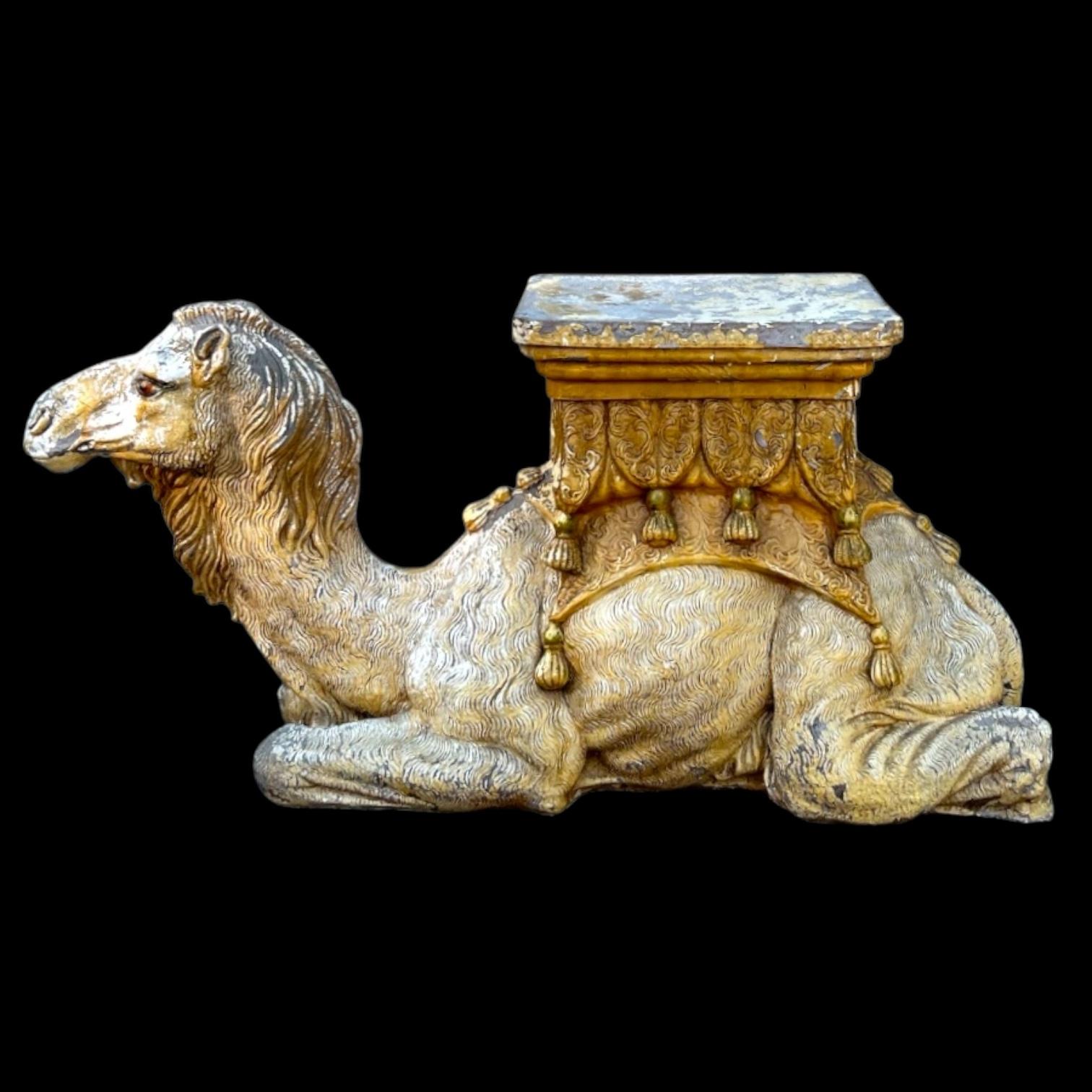 This is a large scale Hollywood Regency cast camel garden seat or stool. It is composition. The camel is unmarked but has quite a bit of garden patina. The colors are mustard and greys. 