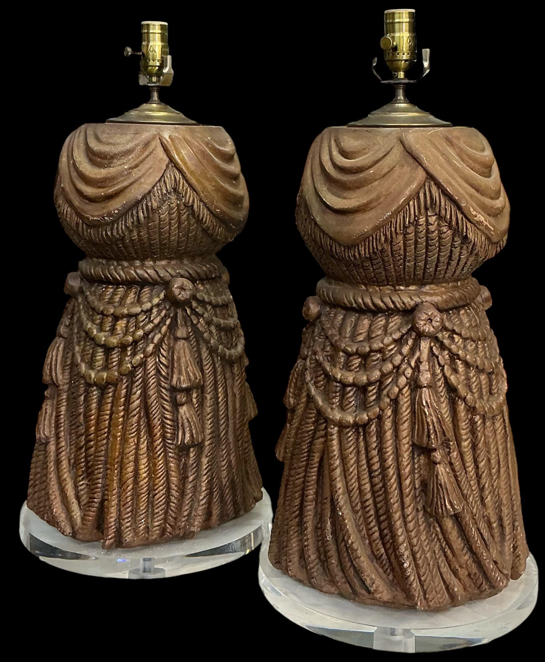 Es handelt sich um ein Paar vergoldete Hollywood-Regency-Lampen mit Quasten auf Lucit-Sockeln. Die Verkabelung ist neu. Der Körper hat eine allgemeine Patina, die Quasten sind eine vergoldete Komposition. 
