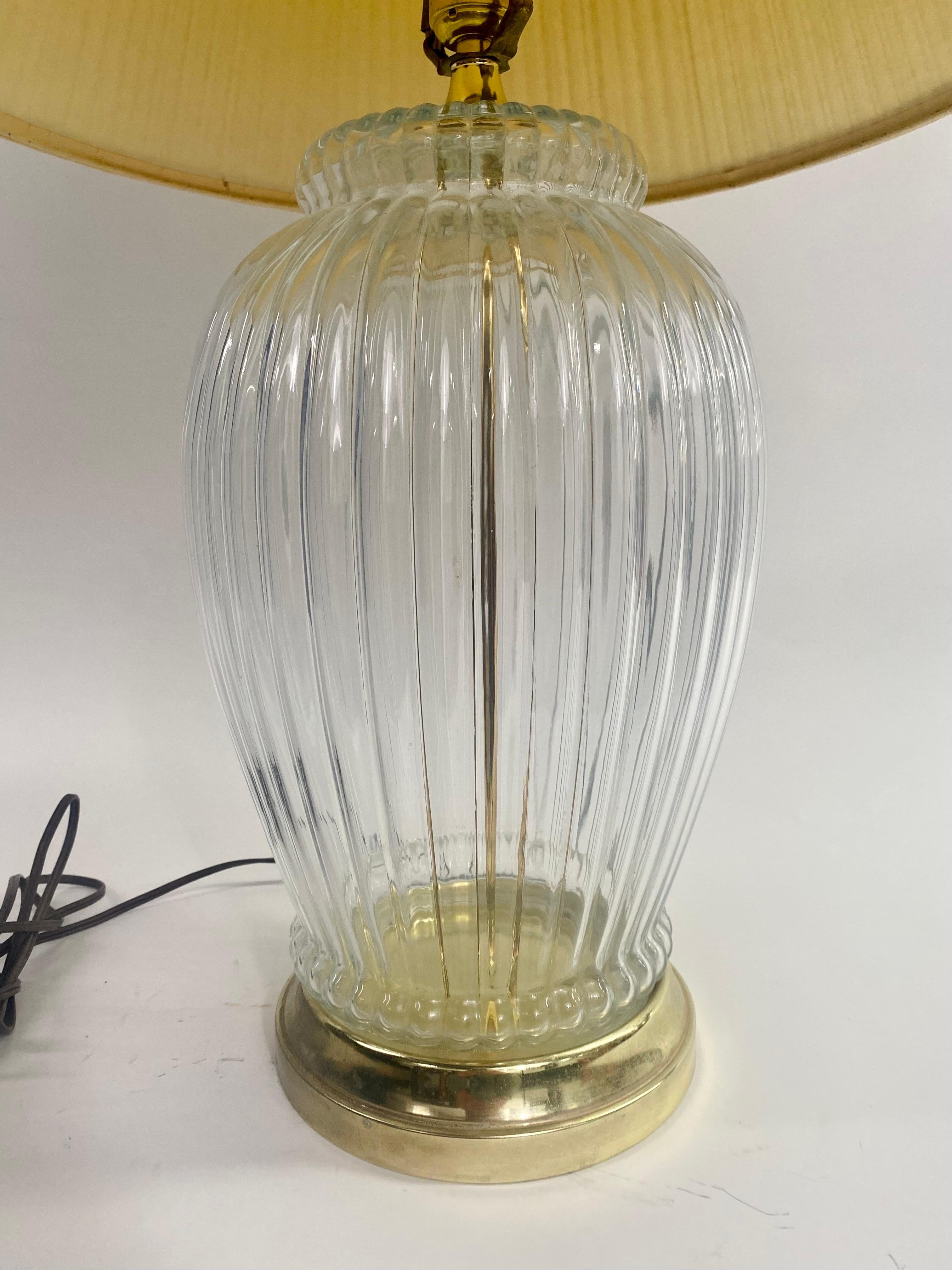 An elegant Hollywood Regency style table lamp featuring a pleated glass oval body. A brass rod attaching the socket to the round solid brass base. The mid-century table lamp is classy and will elevate the style of any room. The lamp takes one