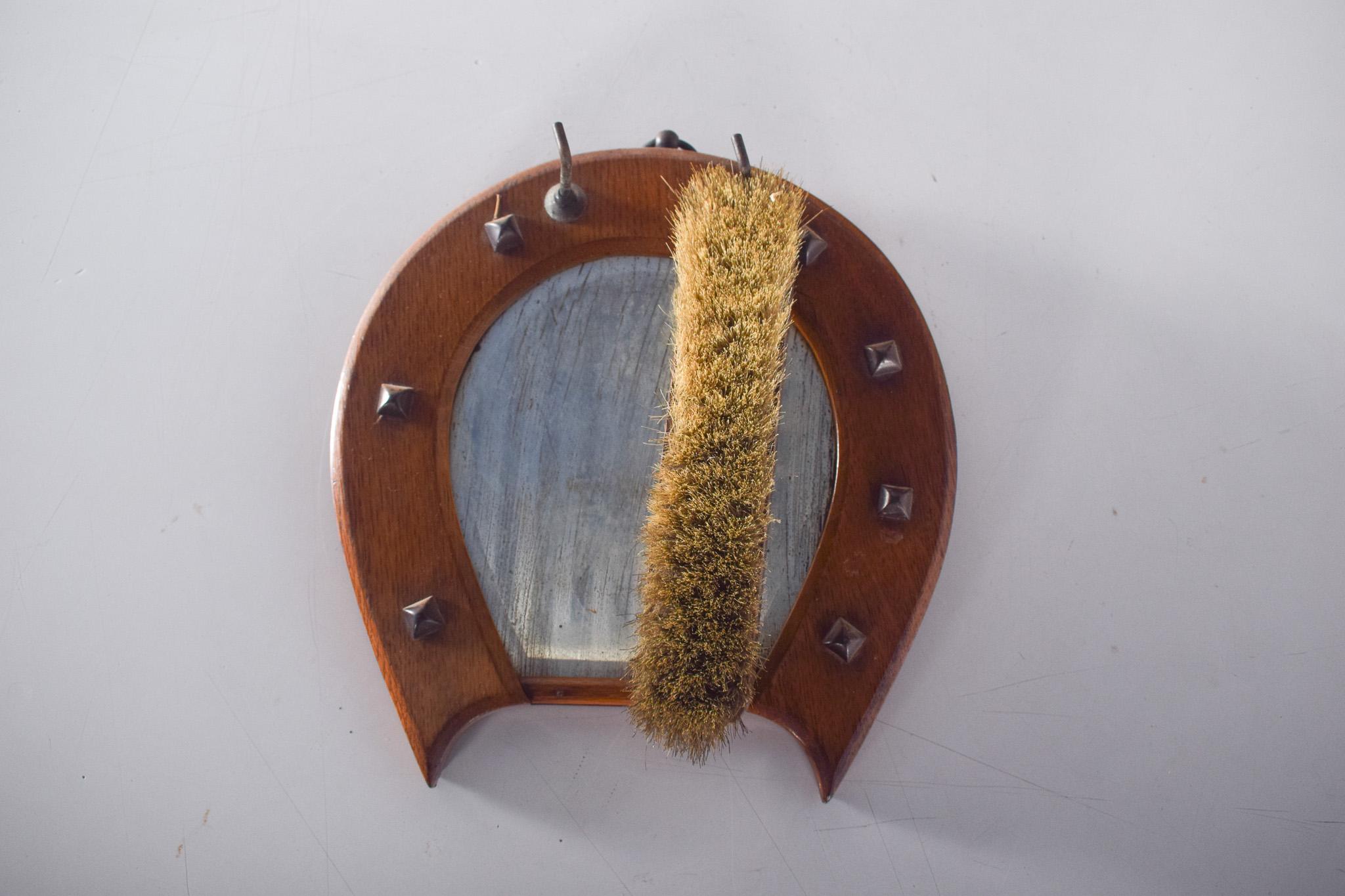 Horseshoe-shaped brush hanger. A rustic and functional piece, ideal for vintage or country environments. It has a horseshoe-shaped base made of varnished wood, which gives it a decorative look. The wooden frame is decorated with metal studs in a