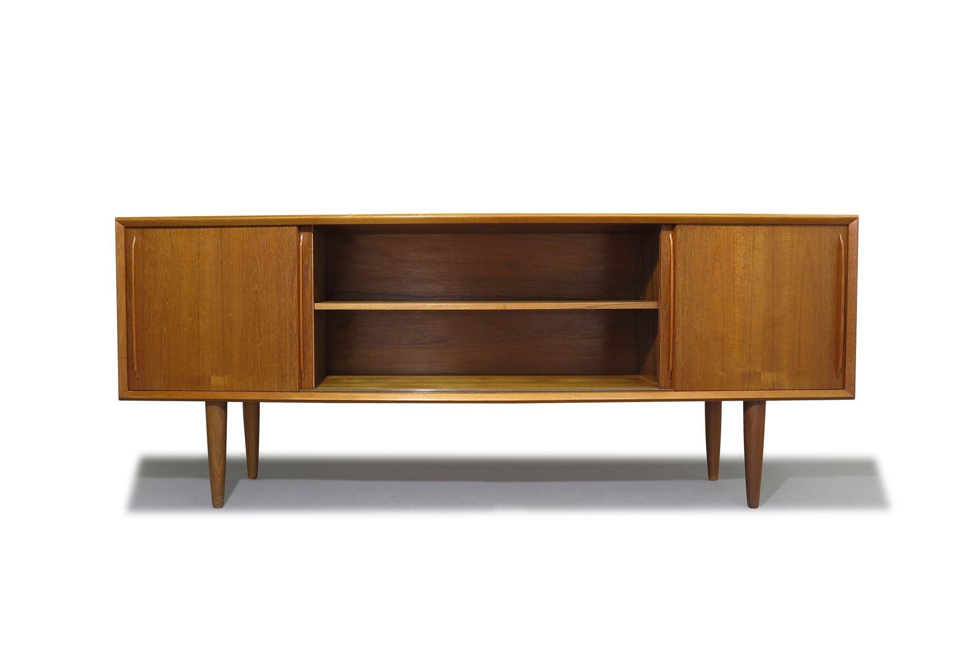 Restored H.P. Hansen teak credenza, crafted from teak, features mitered corners and a bow-curved front with four sliding doors, each with sculpted pulls. The doors open to reveal a series of drawers and adjustable shelves. The credenza has undergone