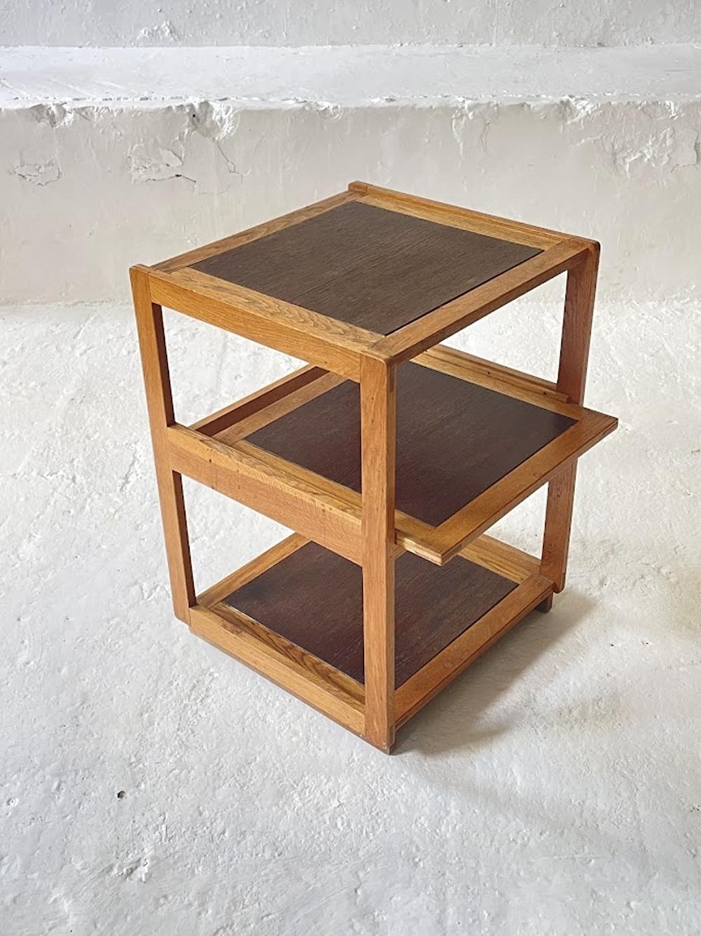 Esta distintiva pieza en forma de cubo de tres niveles muestra un armazón de roble macizo combinado con superficies de chapa de roble, destacando la geometría minimalista y la elegancia funcional. Diseñada como mesa auxiliar versátil, también puede