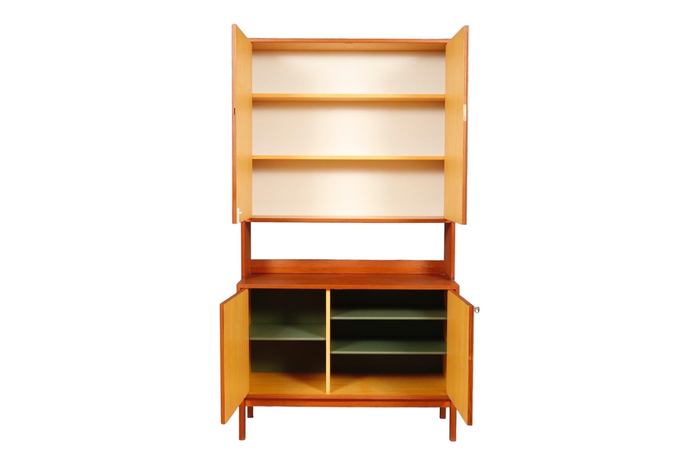 A mid-century hutch cabinet in teak. Upper and lower cabinets house shelves, the interior of the lower cabinet is painted sage. Cabinet doors have a decorative paneled construction.