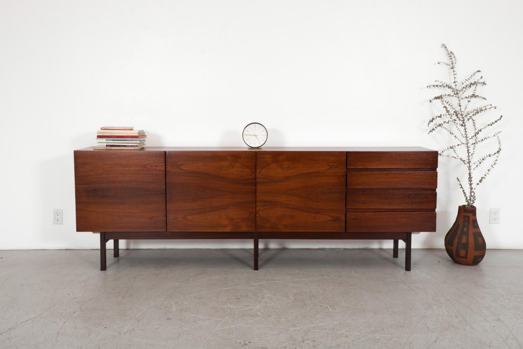 Mid-Century Ib Kofod-Larsen style rosewood credenza. The credenza has a gorgeous book matched figuration and sits atop a wood base with six rectangular legs and ash interior. An elegant storage piece consisting of four green felt lined stacked