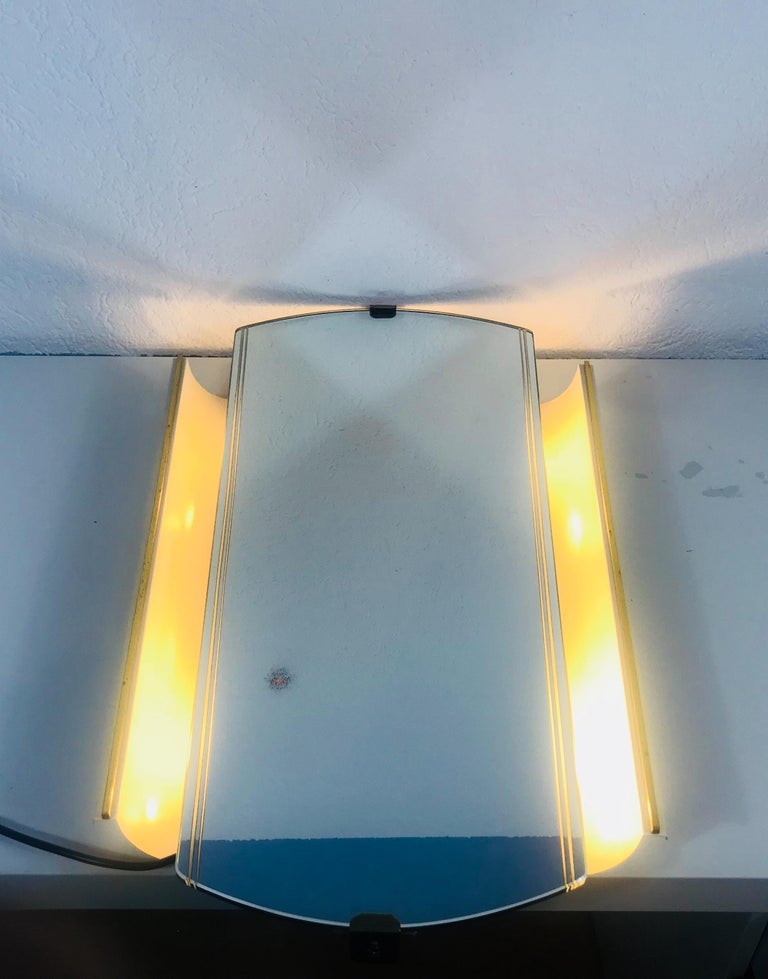 An illuminated wall mirror from the German manufacturer Hillebrand lighting. It was made in the 1950s. The mirror has a beautiful midcentury design. The body is made of metal and brass. There are E14 light bulbs inside the frame. The mirror is in a