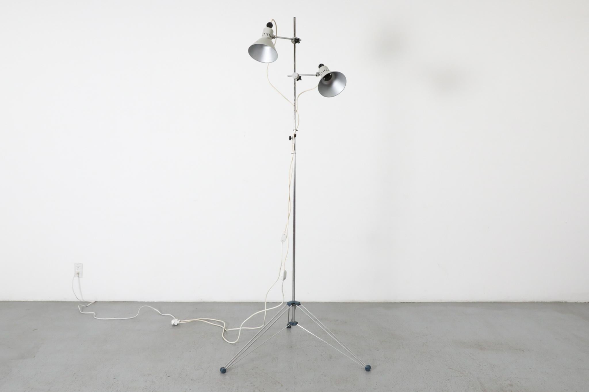 Lampada da terra da studio industriale di metà secolo con base a treppiede pieghevole. Ha sottili dettagli blu ed è dotato di due paralumi in metallo smaltato grigio. Entrambe le luci sono regolabili. In condizioni originali, con usura visibile, tra