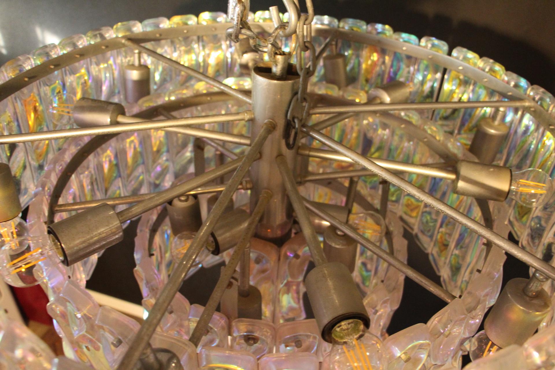 Questo favoloso lampadario è incredibile: i suoi colori cambiano a seconda della luce e dell'ambiente circostante.
Le sue placche in vetro di Murano cambiano colore dal bianco iridescente al giallo, verde, blu, rosa e viola.
Presenta 4 livelli ed