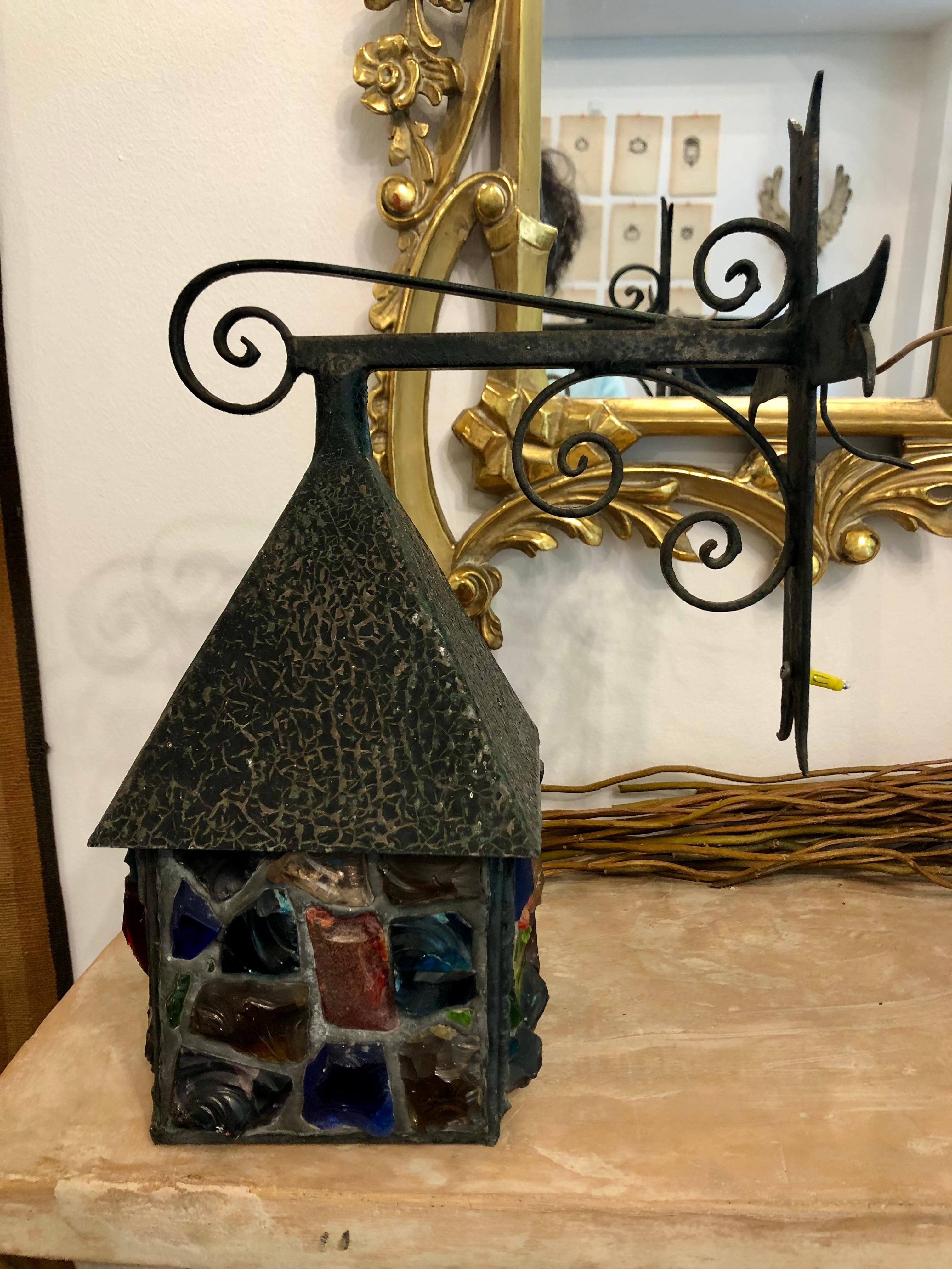 A wonderful Arts & Crafts style, mid-century lantern by English glass artist Peter Marsh. Leaded multicoloured glass  accented by Arts & Crafts style wrought iron scrollwork mounts.
Peter Marsh is known for his chunky, house shaped lamps, with jewel