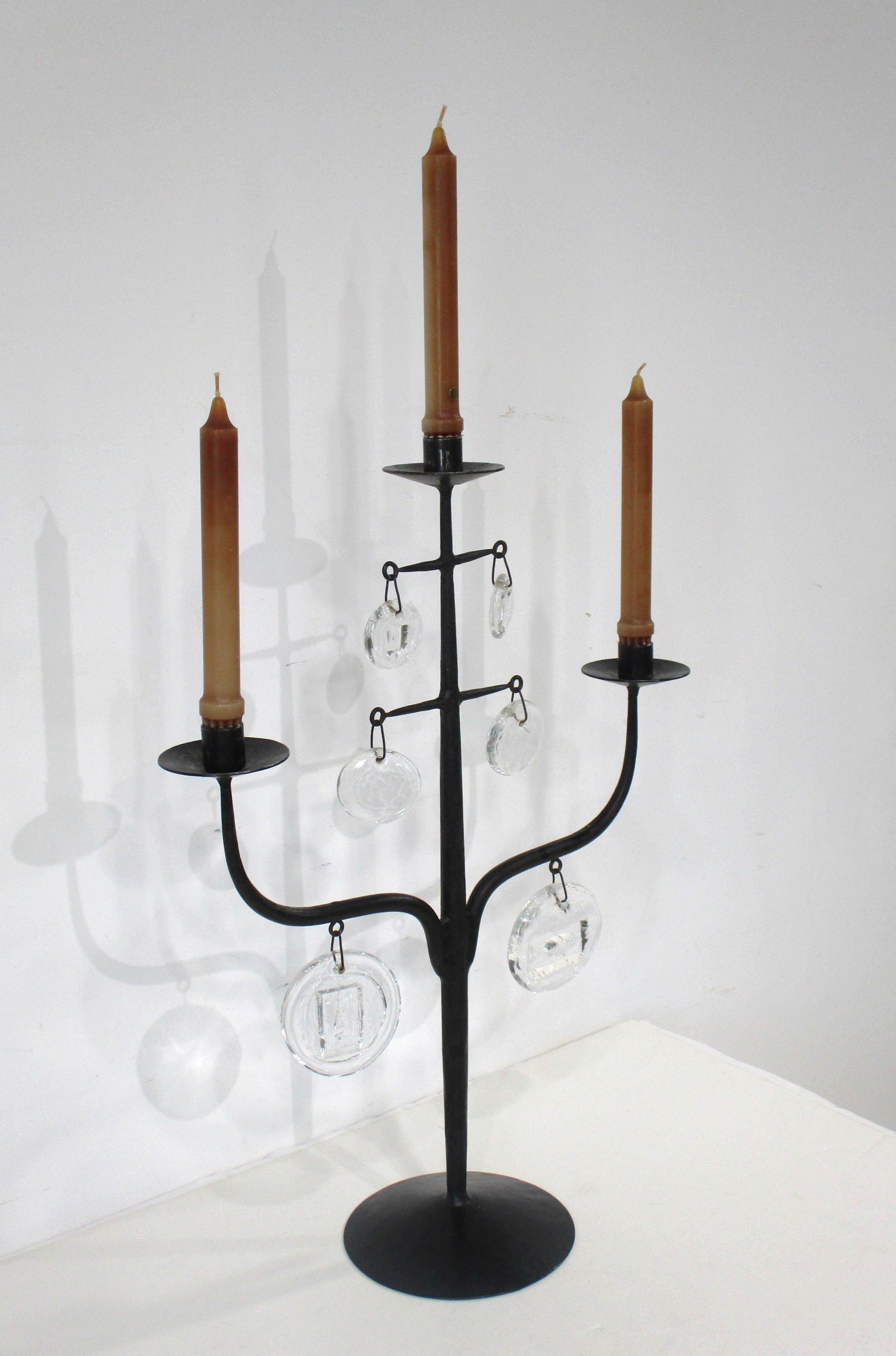 A Mid Century handcrafted black iron three stick candelabra with handblown glass hanging rondels some having faces and fish designs by Boda . A great mix of modern and folk art , made in Sweden and designed by Erik Hoglund in the early 1950's .    